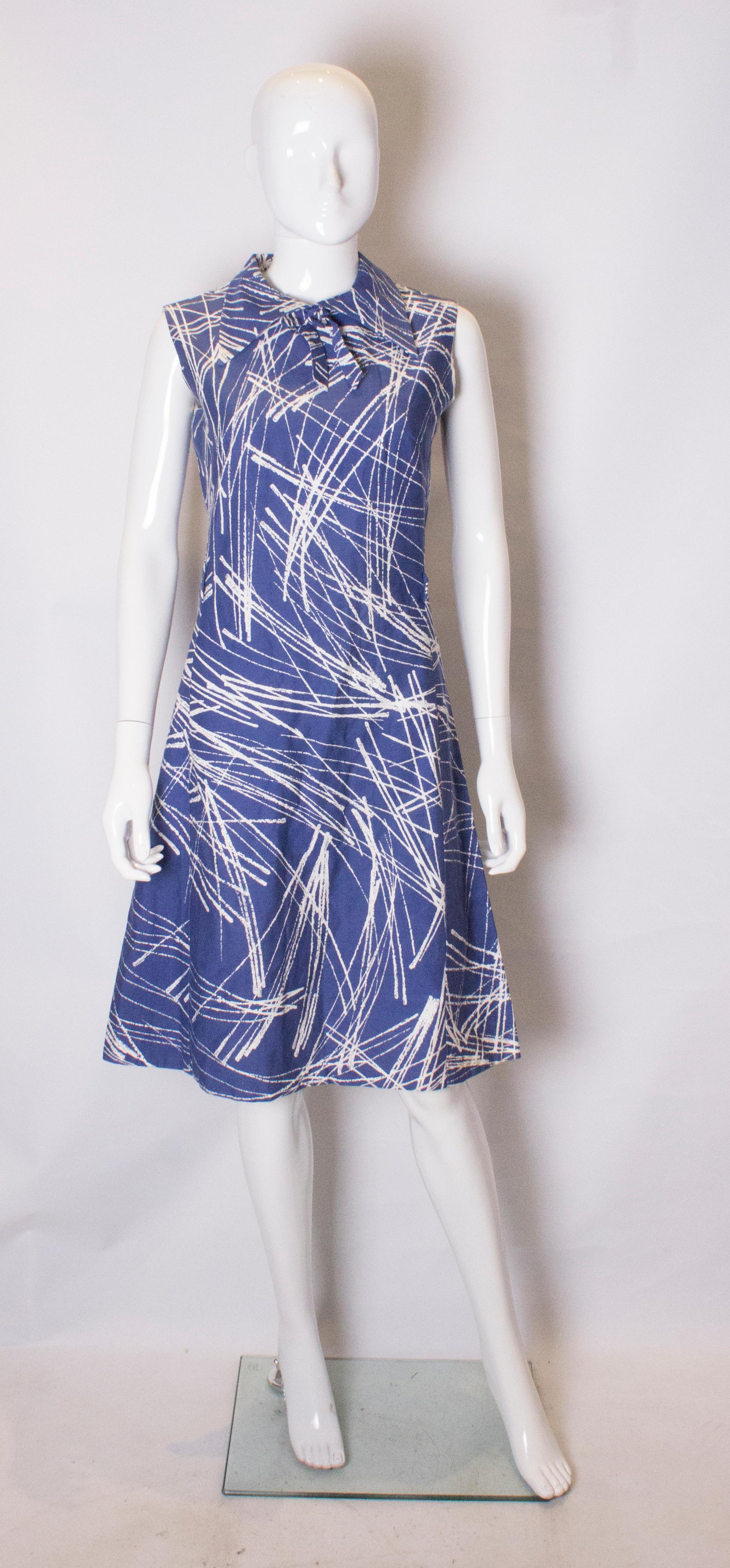 A vintage dress by Montigo Bay day dress. The dress has  a blue background with white print. It has a collar and tie at the neck and a central back zip.
