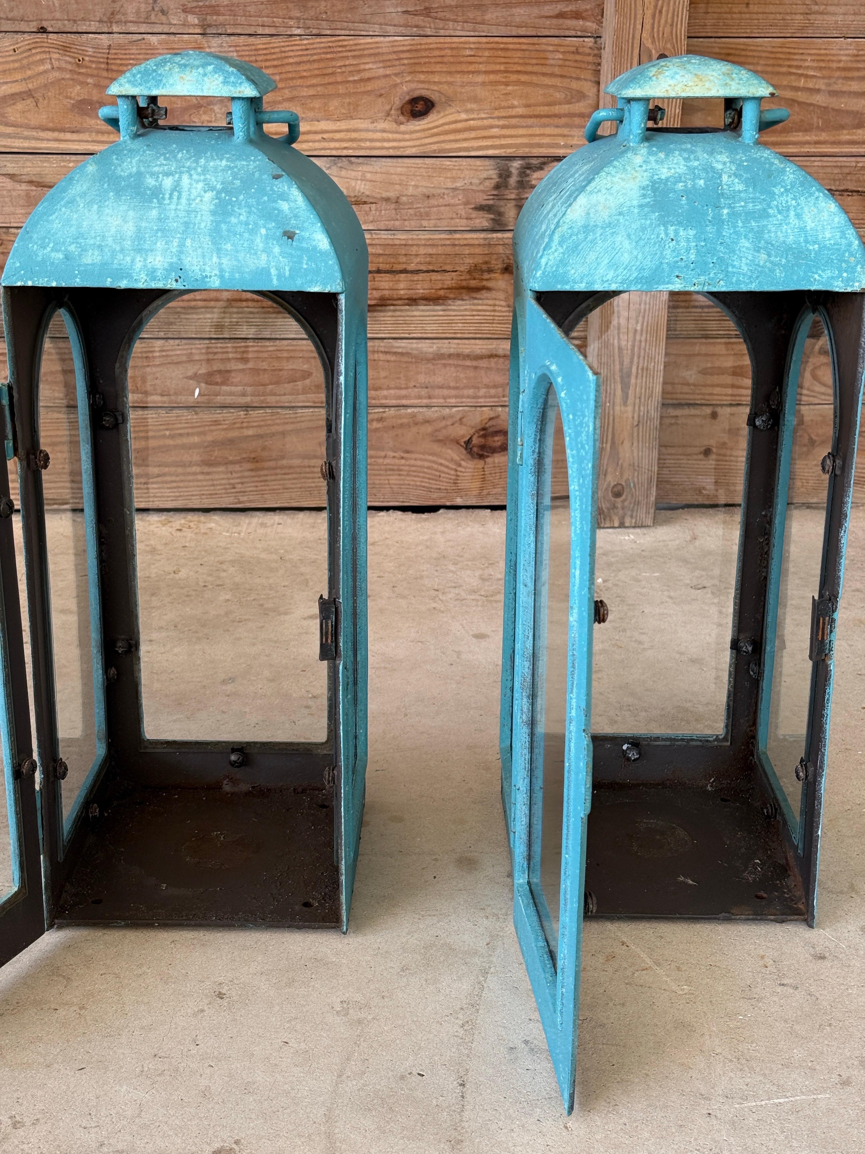 Una coppia monumentale di lanterne vintage in ghisa con una finitura turchese invecchiata e pannelli di vetro ad arco. Eccezionalmente pesante con strati di fascino rustico e patina dovuta all'età e alla precedente verniciatura. Perfetto per dare un