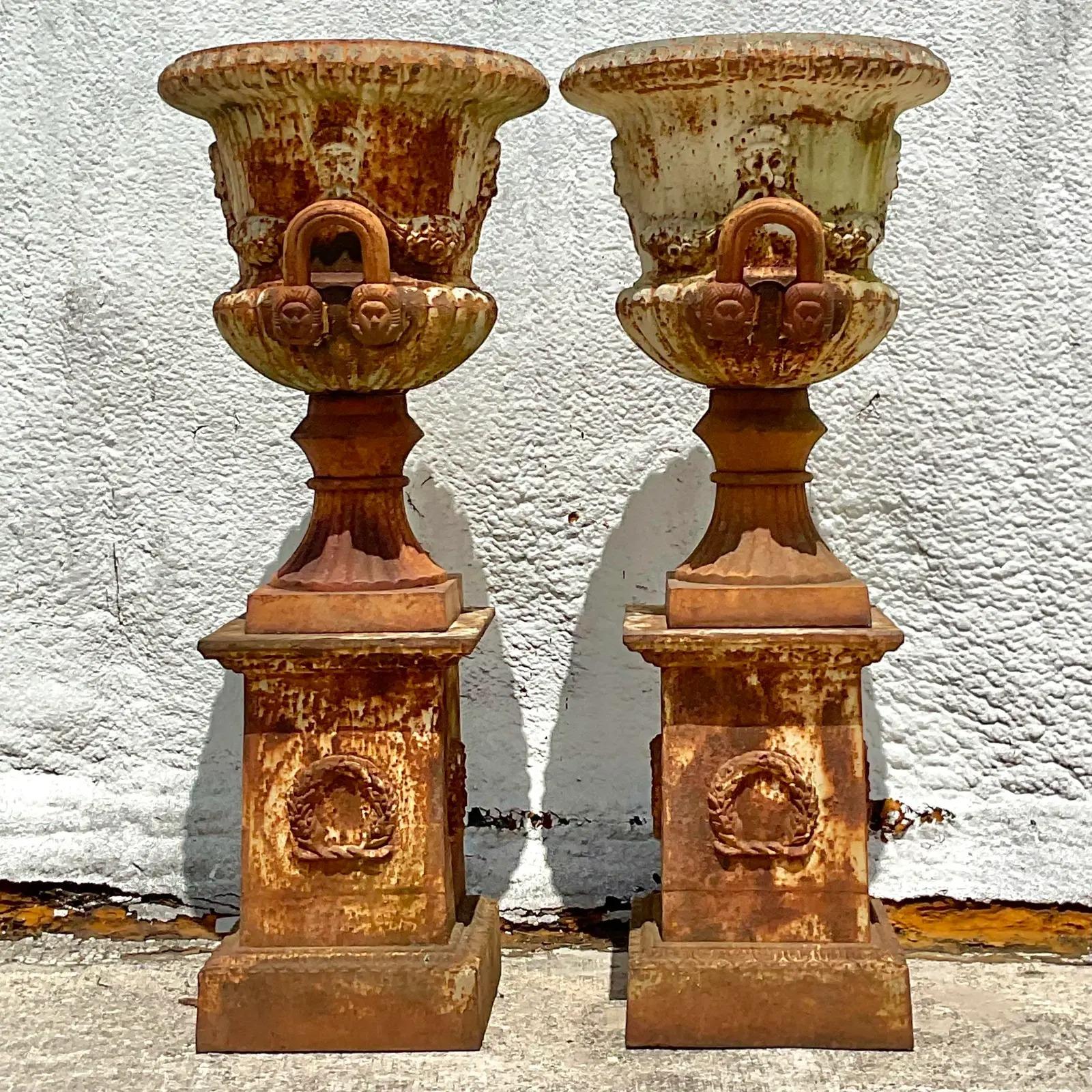 Fantastic pair of vintage Garden urns. Monumental in size and drama. Freestanding urns with swags and garlands and masks that rest on a matching plinth. Tons of good rusty patina from time. Acquired from a Palm Beach estate.
