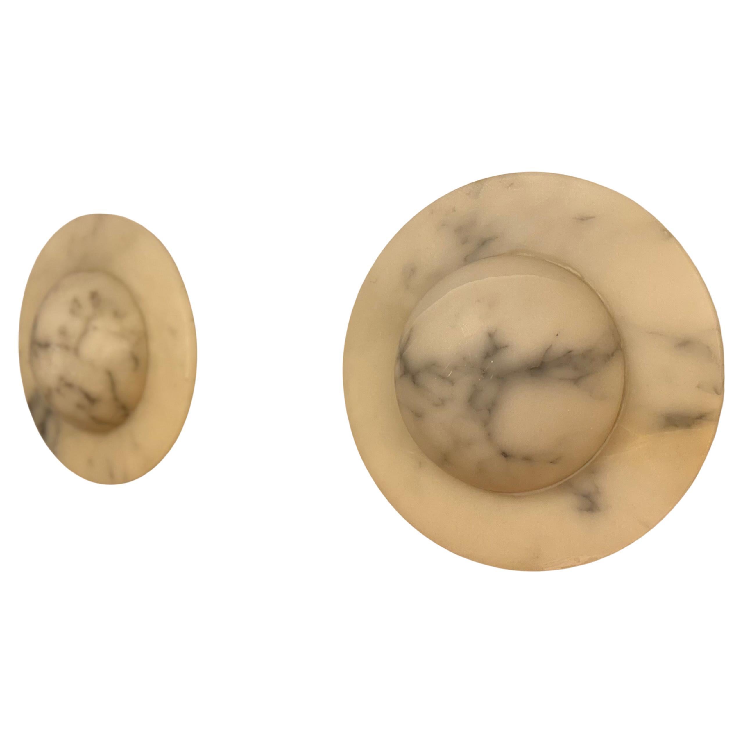 Paire d'élégantes appliques murales en albâtre à motif de lune. Fabriquées en délicate pierre d'albâtre blanche minéralisée, ces appliques orbitales ajoutent une touche de sophistication à n'importe quelle pièce. Chaque luminaire peut accueillir