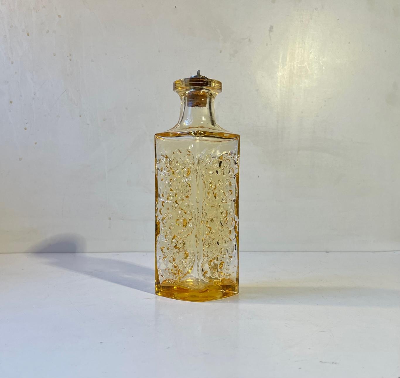 Small 0.5 liter liquor decanter in ocre-toned glass. It is made from handblown glass and its texture imitates the surface of the moon. It has its original stopper in brass and cork from Holmegaard. It was made at Holmegaard in Denmark during the