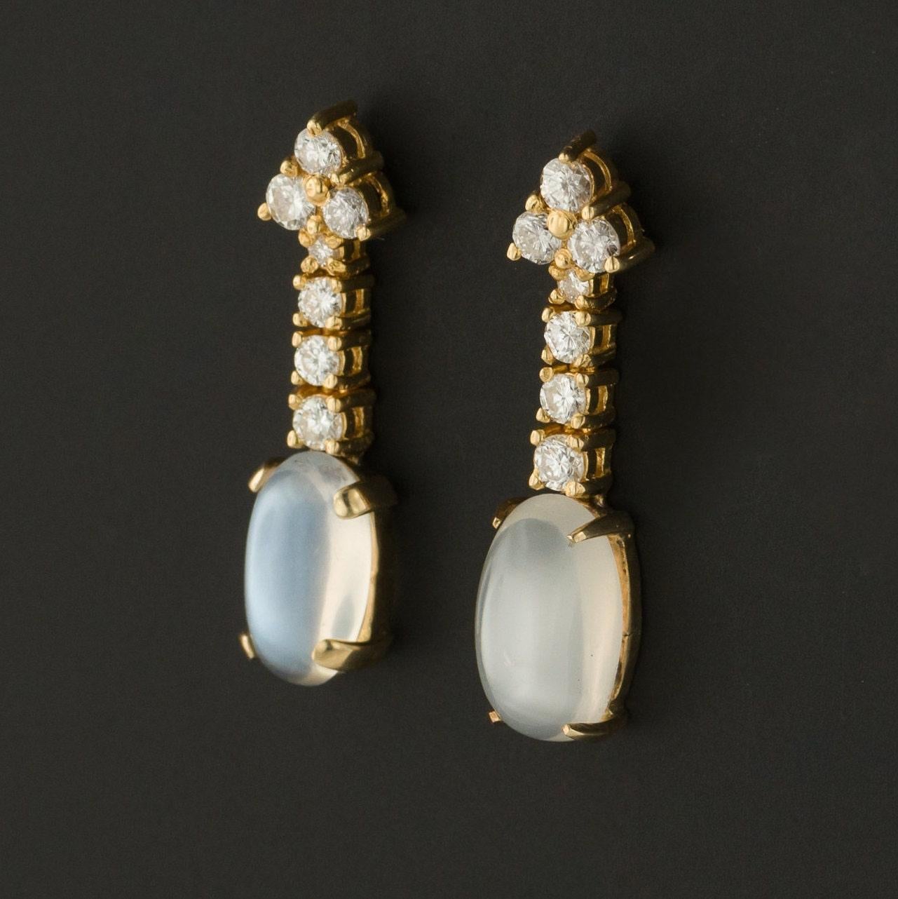These playful 1970s era earrings are rendered in 18k gold. Each earring consists of a three diamond surmount and a cascade of four hinged diamonds ending in an iridescent moonstone drop. The diamonds are modern round brilliant cut and the total