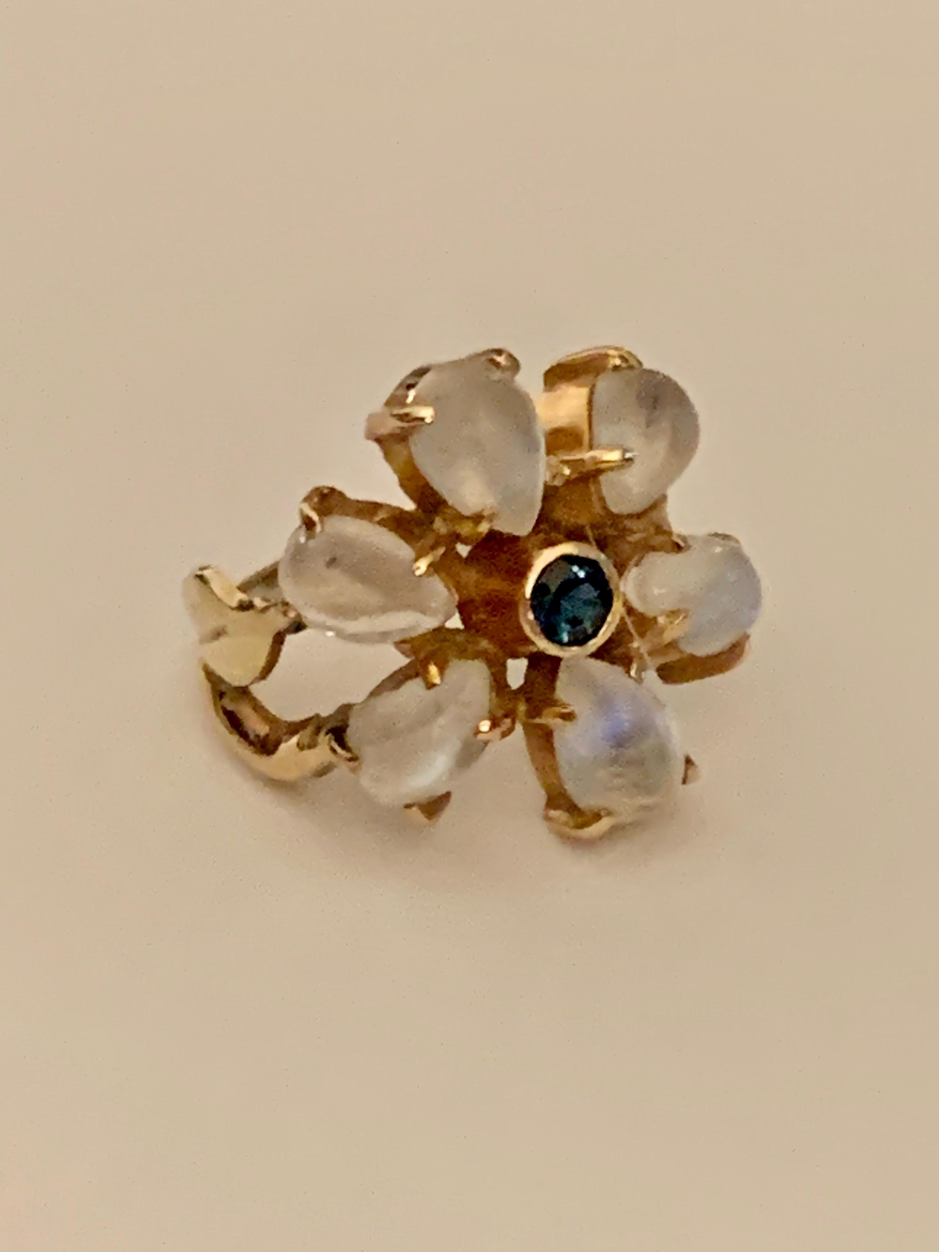 This ring is a moonstone-lovers dream.  There are six tear drop shaped moonstones surrounding a blue Sapphire in the center of the ring. 
The setting is 14 karat yellow Gold and features a split shank on each side of the center moonstone