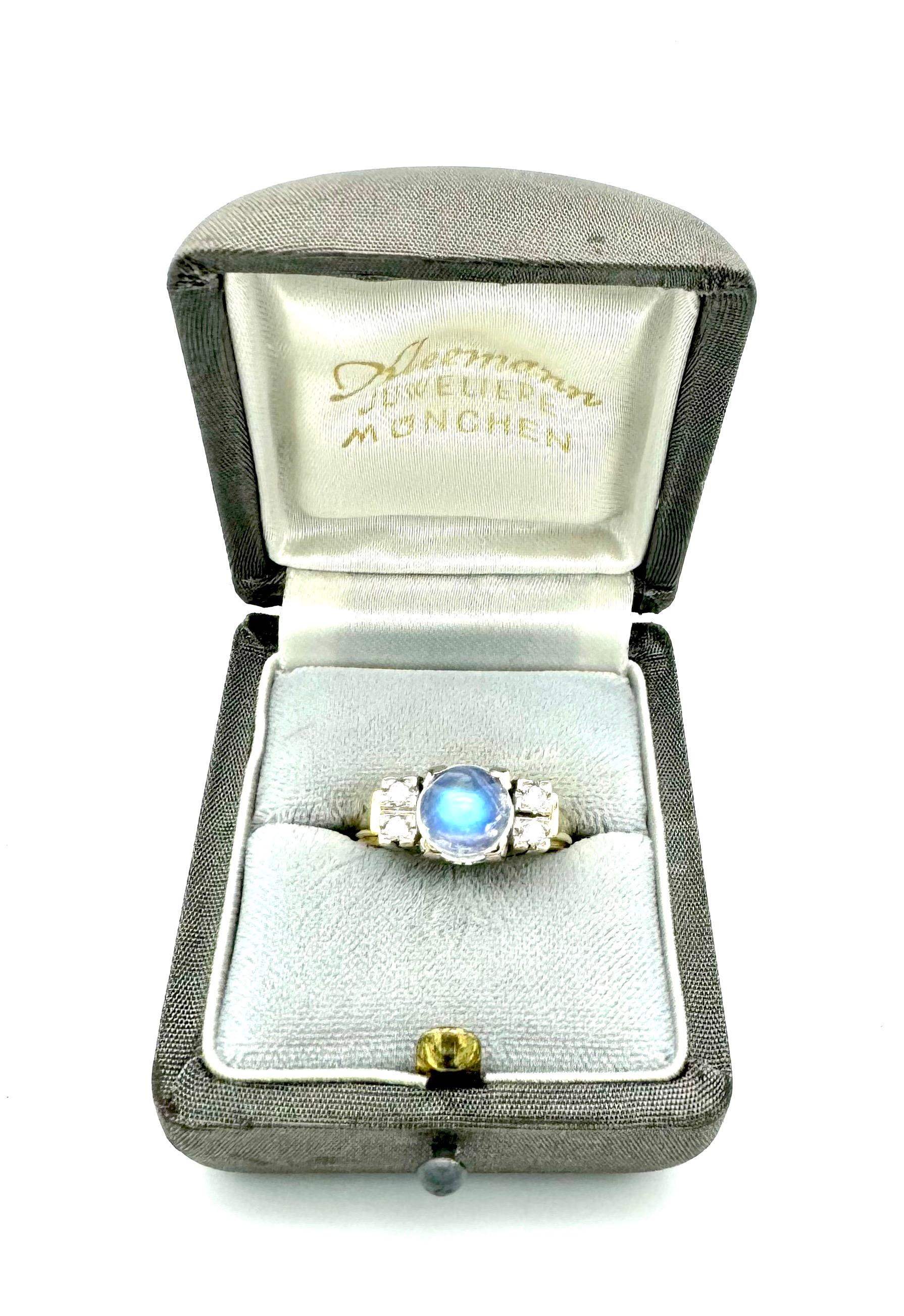 This ring was created in 1970 ca. out of 14K white and yellow gold. In the centre of the ring head there is an intense blue moonstone cabochon in a setting with four claws that form the corners of an imaginary square. To either side of the moonstone