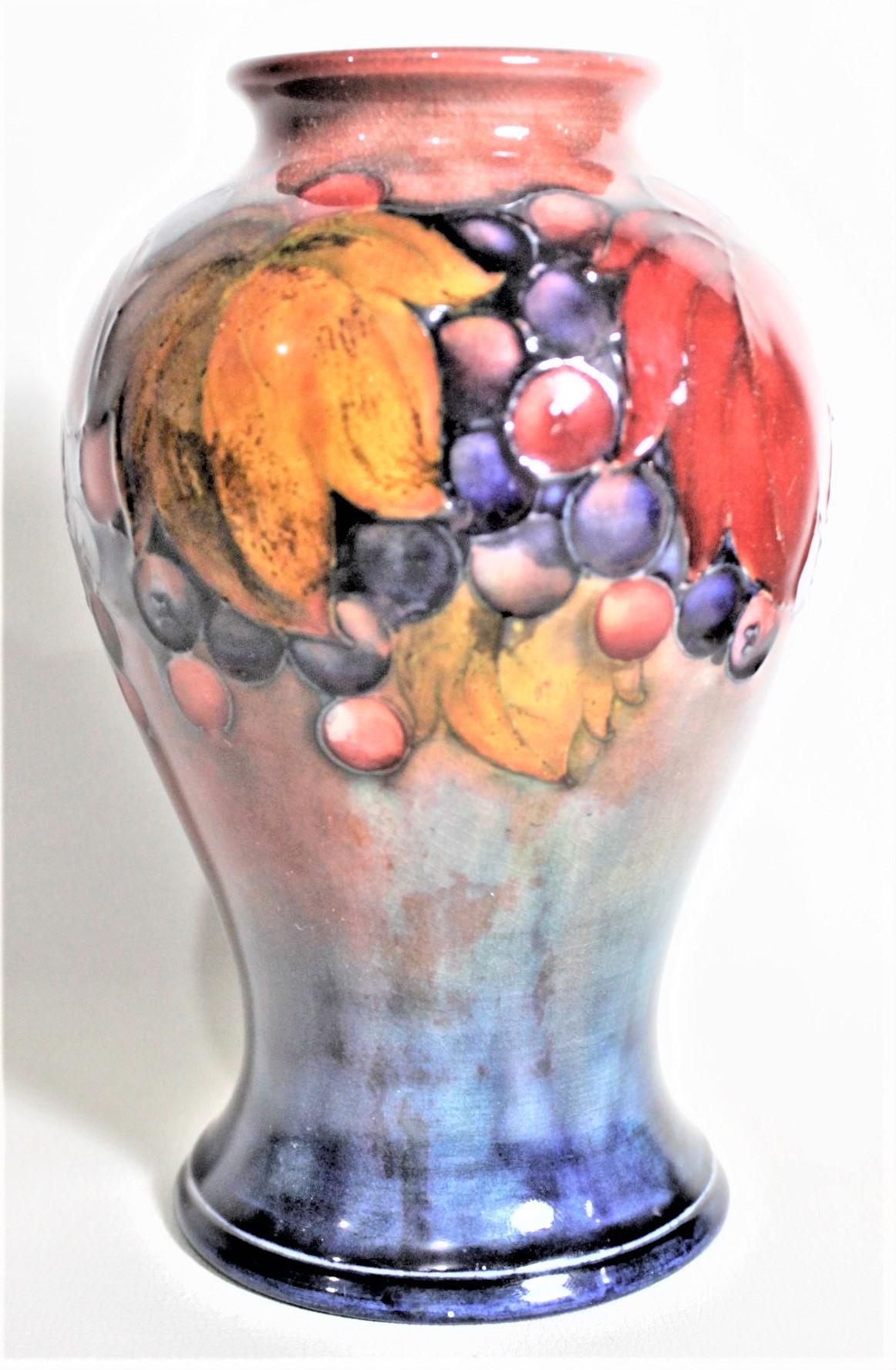 This art pottery vase was done by the Moorcroft Pottery company of England in circa 1939 using their 'flambe' glaze with their 'Leaf & Berry' pattern. The one side of the vase is done is vibrant colors with touches of red, and the reverse side shows