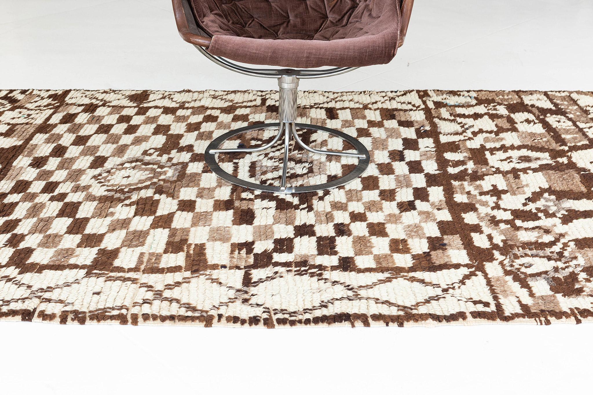 Ivory ground with rectangular compartment areas of rich brown and tan checkerboard patterns and motifs. This densely filled rug has a feeling of eccentric order. Taking cues from formal rugs as evidenced by the symmetrical composition and central