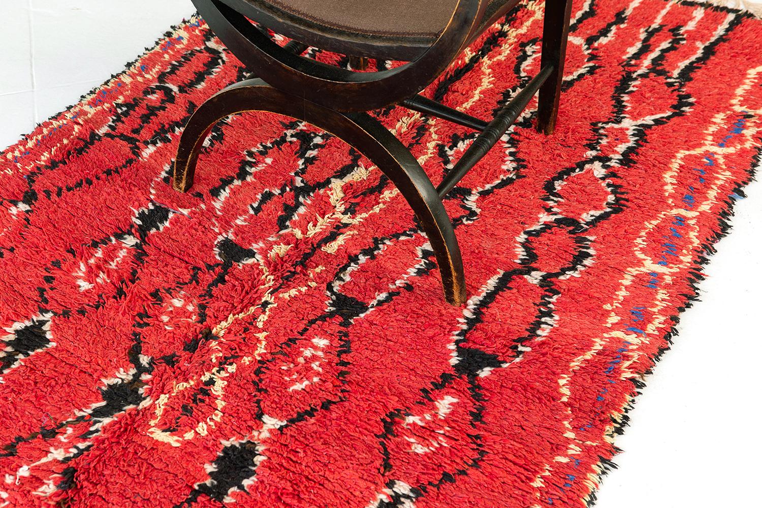 Cherry red pile field with diamond chains rendered in black and ivory wool. Pale gold and cobalt blue elements enlarge the palette and black filled spaces add weight. This is a vivid and graphical composition. A unique vintage tribal rug from the