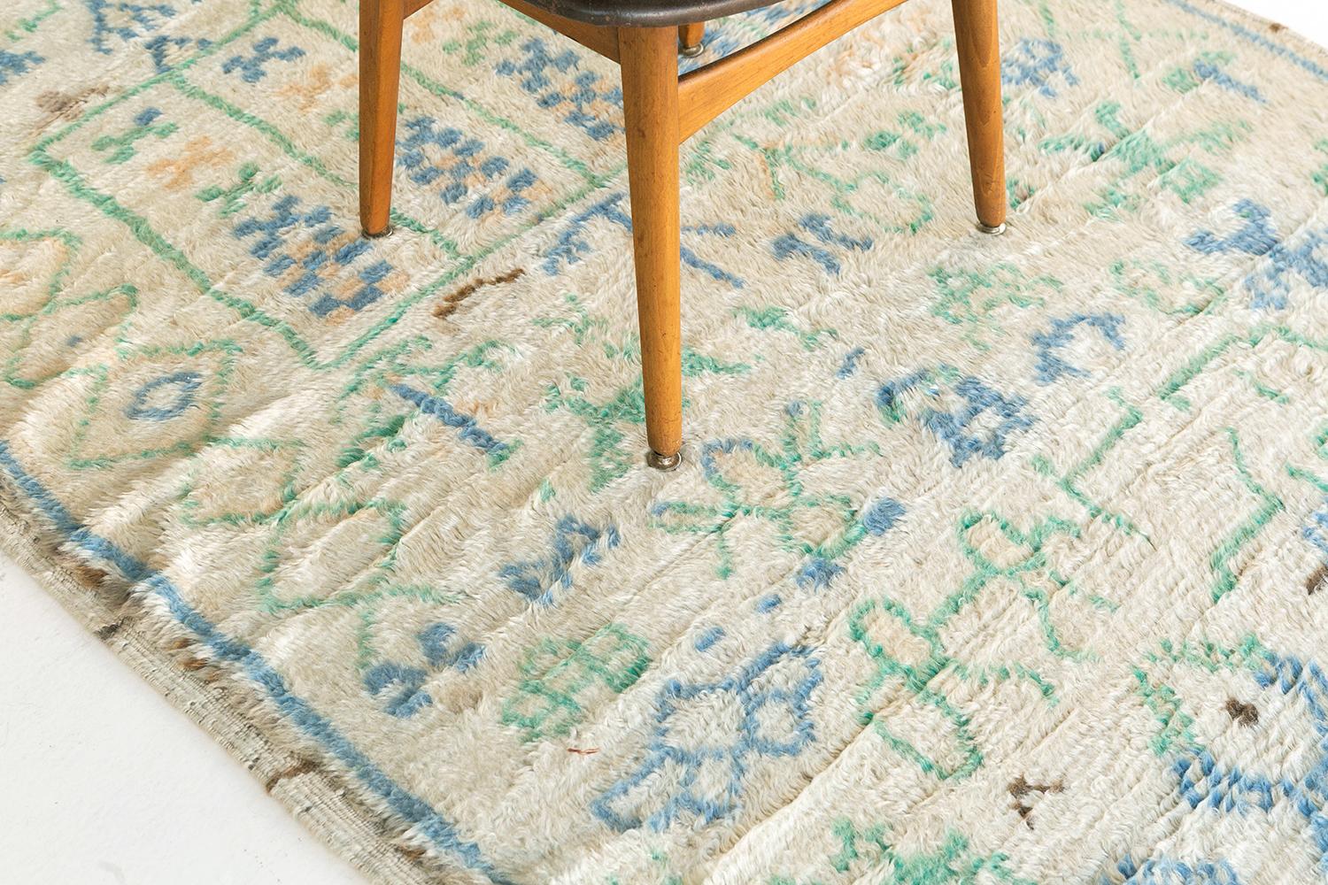 Ivory ground with cheerful azure, emerald, and golden details. Agrarian motifs include human and animal figures. The composition is axial and directional, buzzing with life. A vintage Berber lyric from the Atlas Mountains.

Rug
