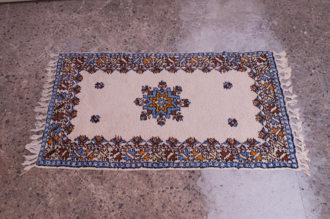 Rabat accent rug in off-white with brown, orange, tan, brown, and blue accent colors, circa 1960s. Central tribal medallion present. Including fringe, measures: L 64