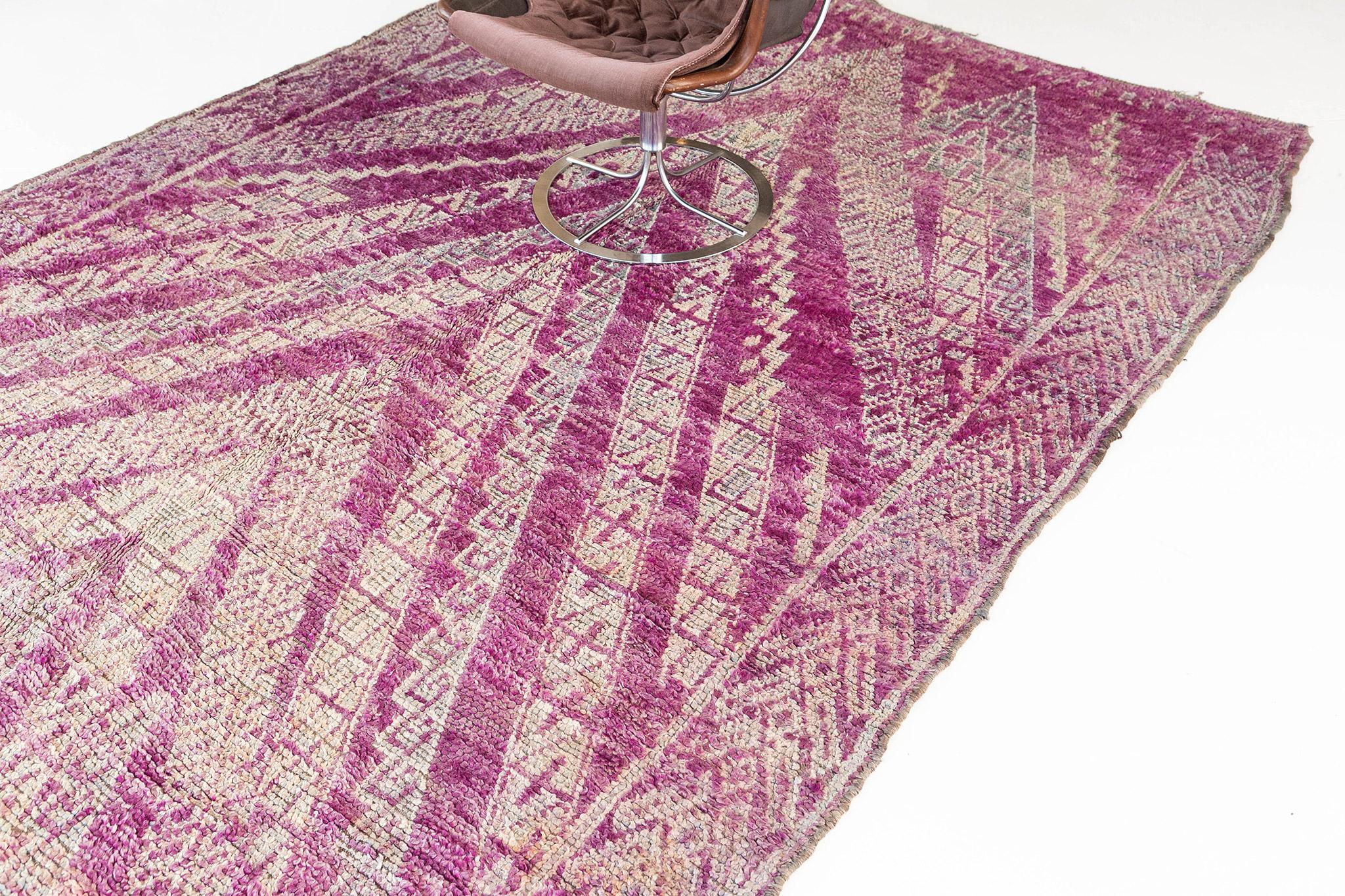 Caractéristique du Beni M'Guild, ce tapis présente un champ magenta vif avec des chevrons traditionnels en saillie de couleur anthracite et taupe, soulignés d'ivoire. Les bordures latérales reprennent la forme du V à une échelle plus petite et plus