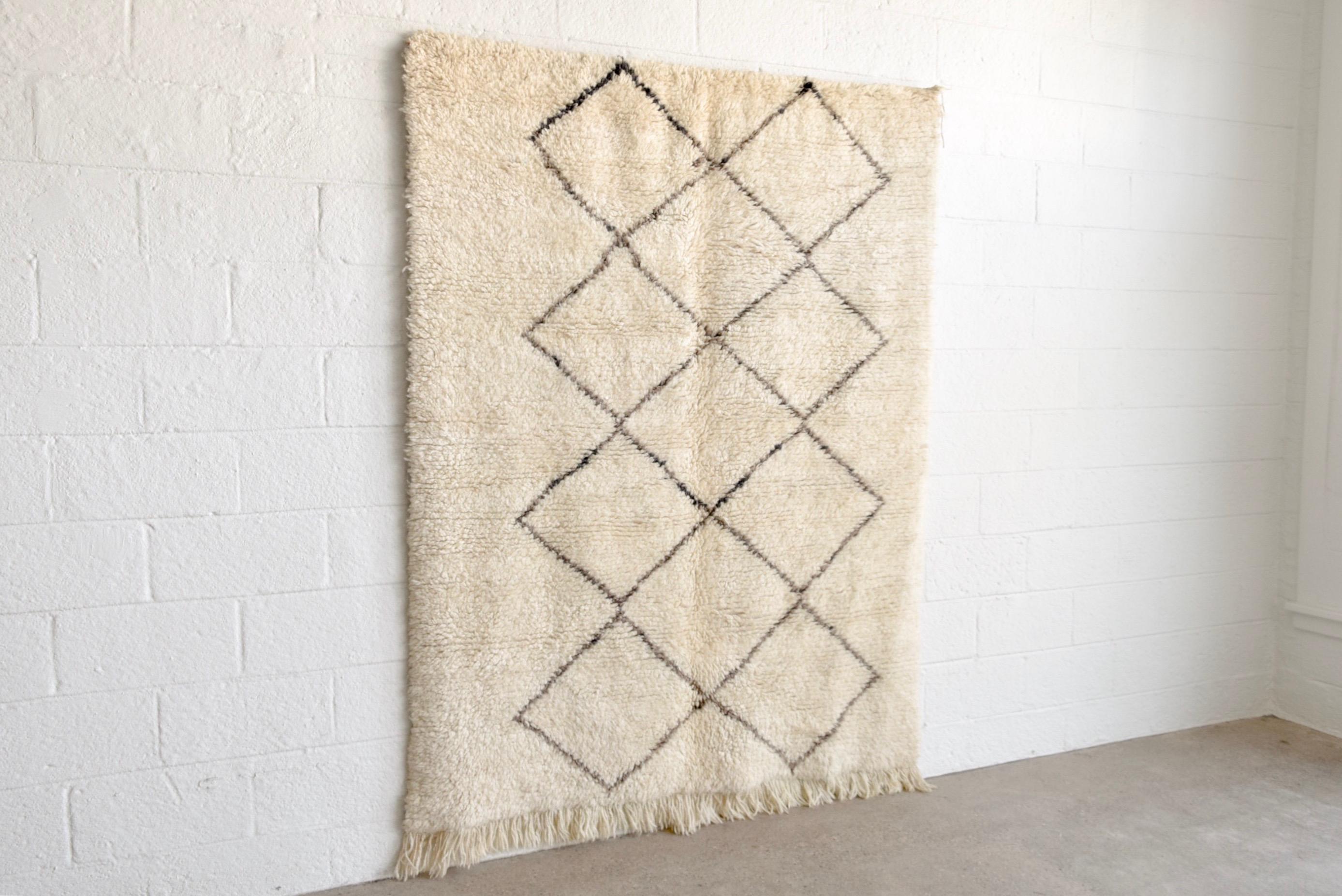 This vintage handwoven Moroccan Berber Beni Ourain area rug features a simple deep charcoal and brown line diamond lattice pattern on a cream field. The thick wool pile is soft and supple and the rug is finished with a natural wool warp fringe to