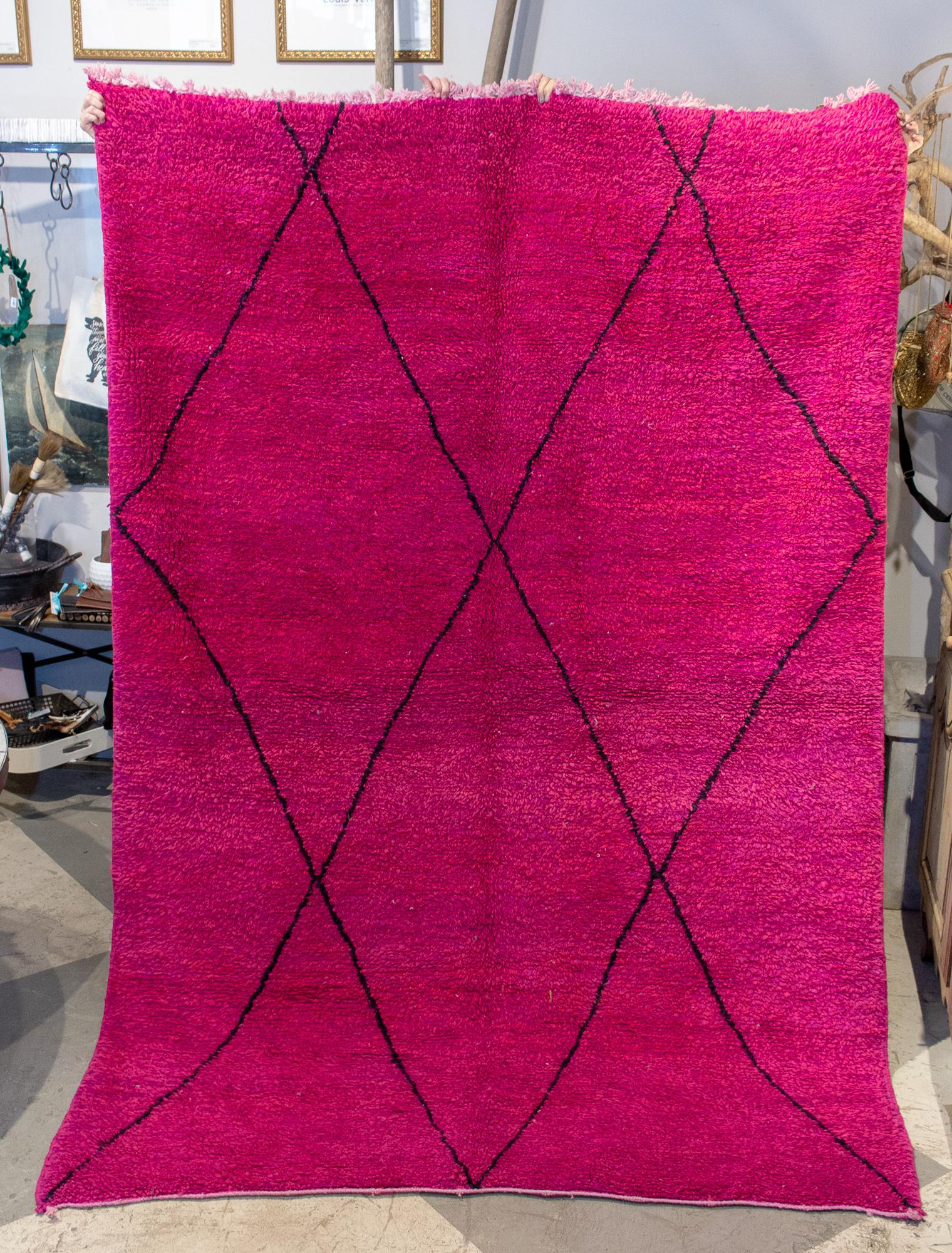 This is a Moroccan Beni Ourain Berber rug sourced in Marrakech. This rug features a hot pink and fuchsia background with black-diamond patterning, as is typical of these rugs. This rug is handmade and features two sides, one flat-woven side for