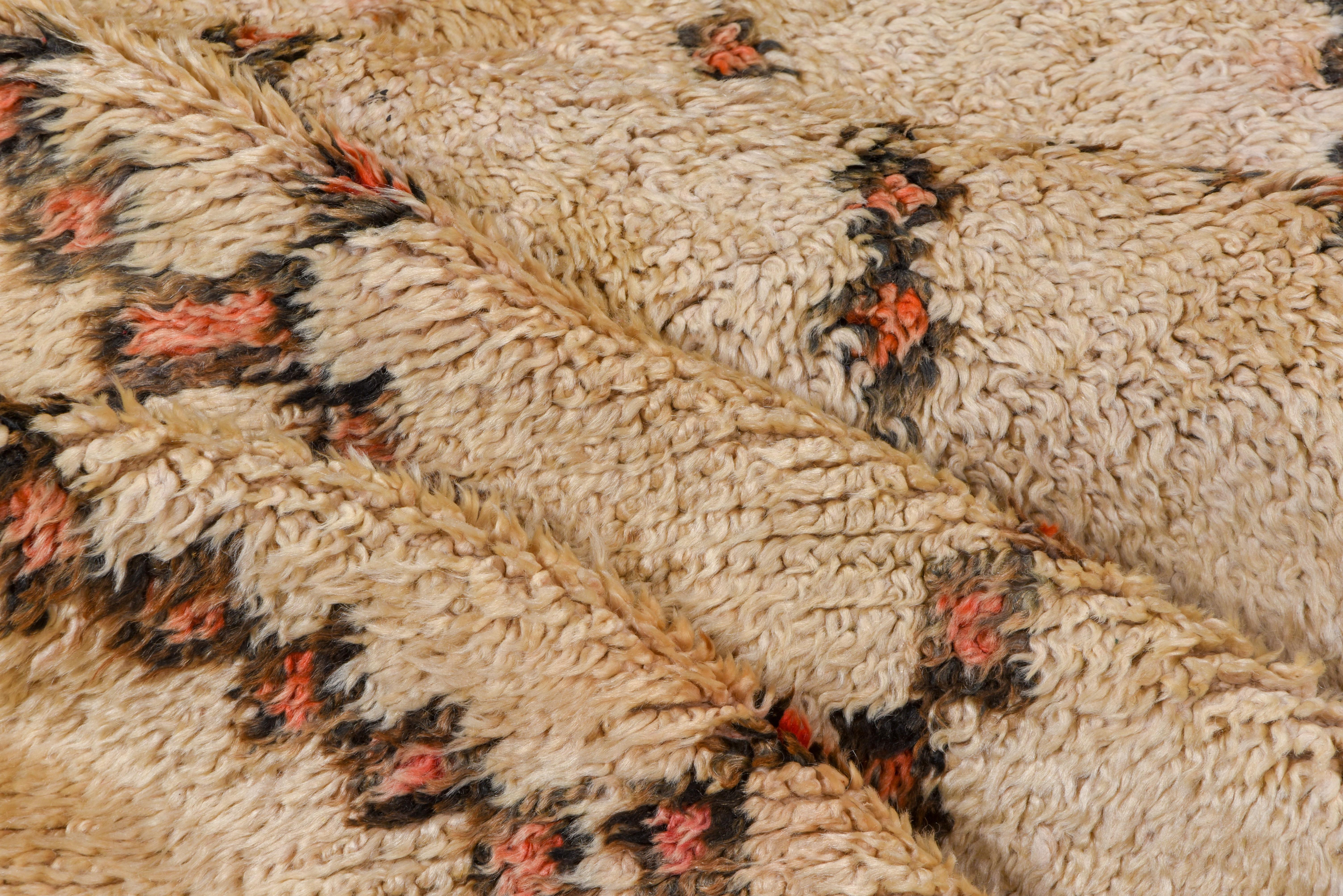 Ce tapis berbère du Haut-Atlas écru et brun foncé présente trois panneaux horizontaux, chacun légèrement différent, du motif caractéristique du losange ouvert en escalier. De petits ornements bruns sont éparpillés au hasard. Diamants corail et brun