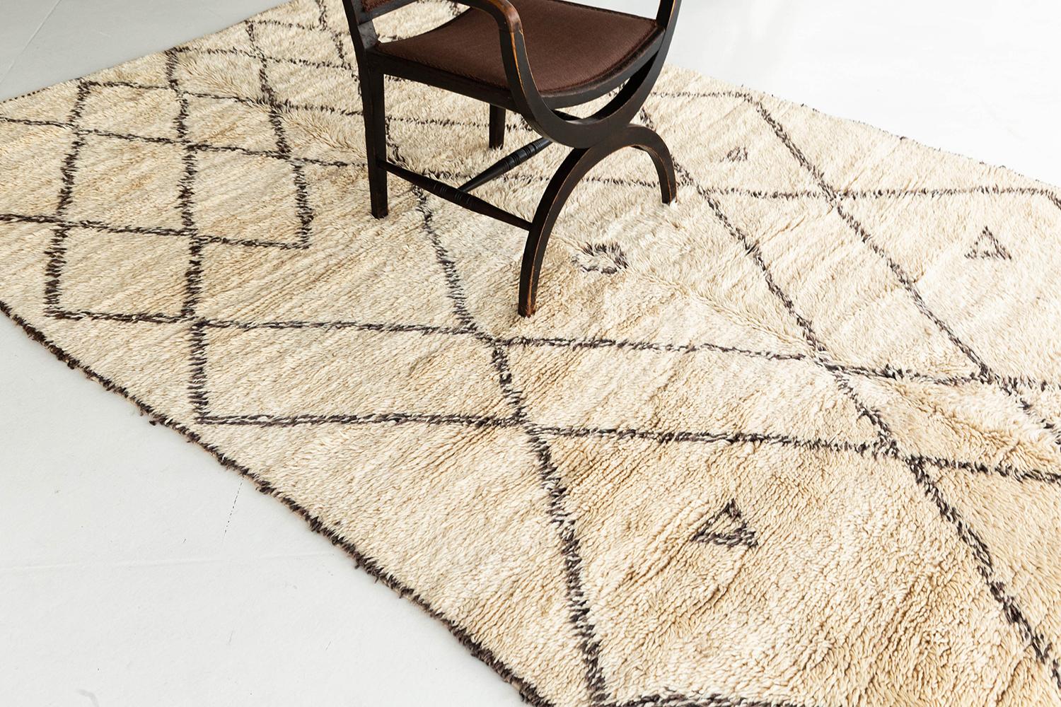 A charming antique Moroccan rug made by the Beni Ourain Tribe. This unique handwoven rug contains traditional line-work latticed throughout the field with symbolic imagery. Beni Ourain tribal rugs are known for their soft black or dark brown