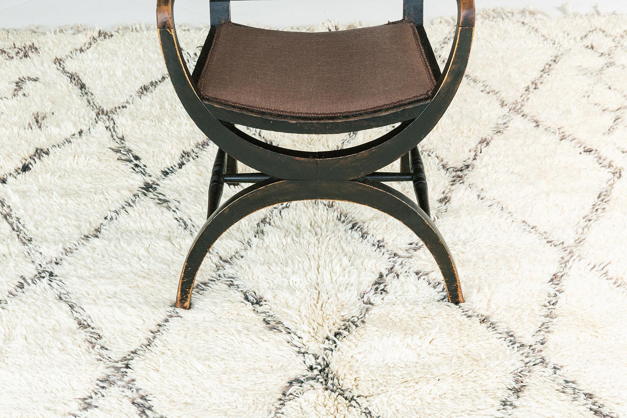 Ivory field with diamond lattice motif rendered in speckled taupe wool. Large scale central design covering the majority of the rug is flanked by smaller repeat motifs-- traditional symbolic elements. A unique vintage rug from the Beni Ourain