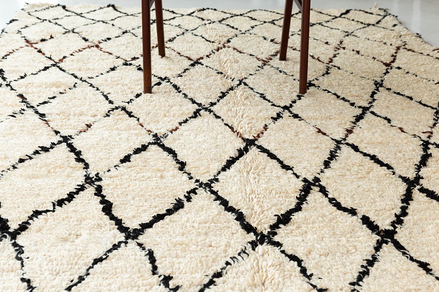 A vintage Beni Ourain tribe Moroccan in ivory with black asymmetrical lines creating a repeating diamond pattern. This rug has a perfect handwoven shag texture and an overall unique design that will add character to any space. The singular colorful