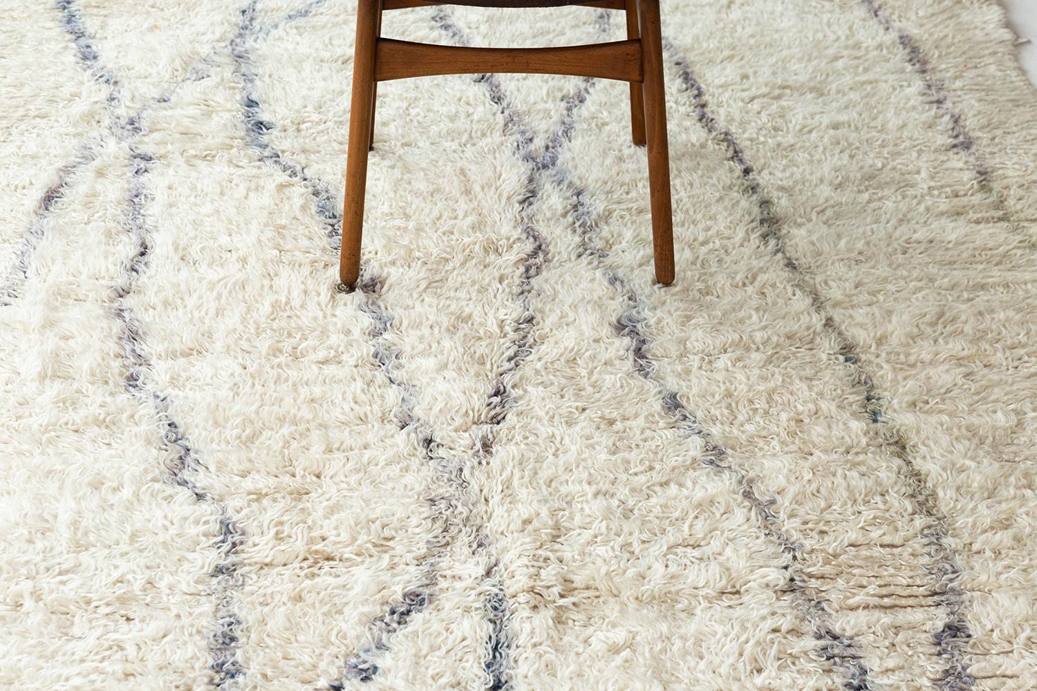 A vintage Moroccan Beni Ourain in the perfect ivory adorned with softened indigo colored asymmetrical lines. The rug's handwoven shag texture adds to the rug's overall excitement and makes for a perfect contemporary. This rug will add character to