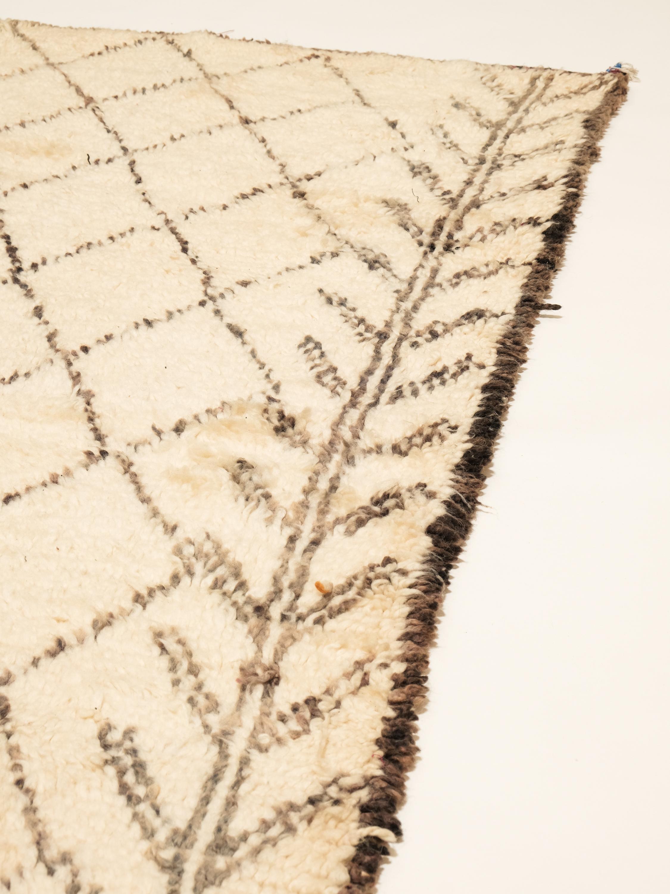 A beautiful vintage Moroccan rug from the Beni Ourain tribe. This charming handwoven wool piece has the perfect sandy ivory color and contains traditional diamond and leaf motifs throughout the field in a golden hue. A one of a kind rug that will