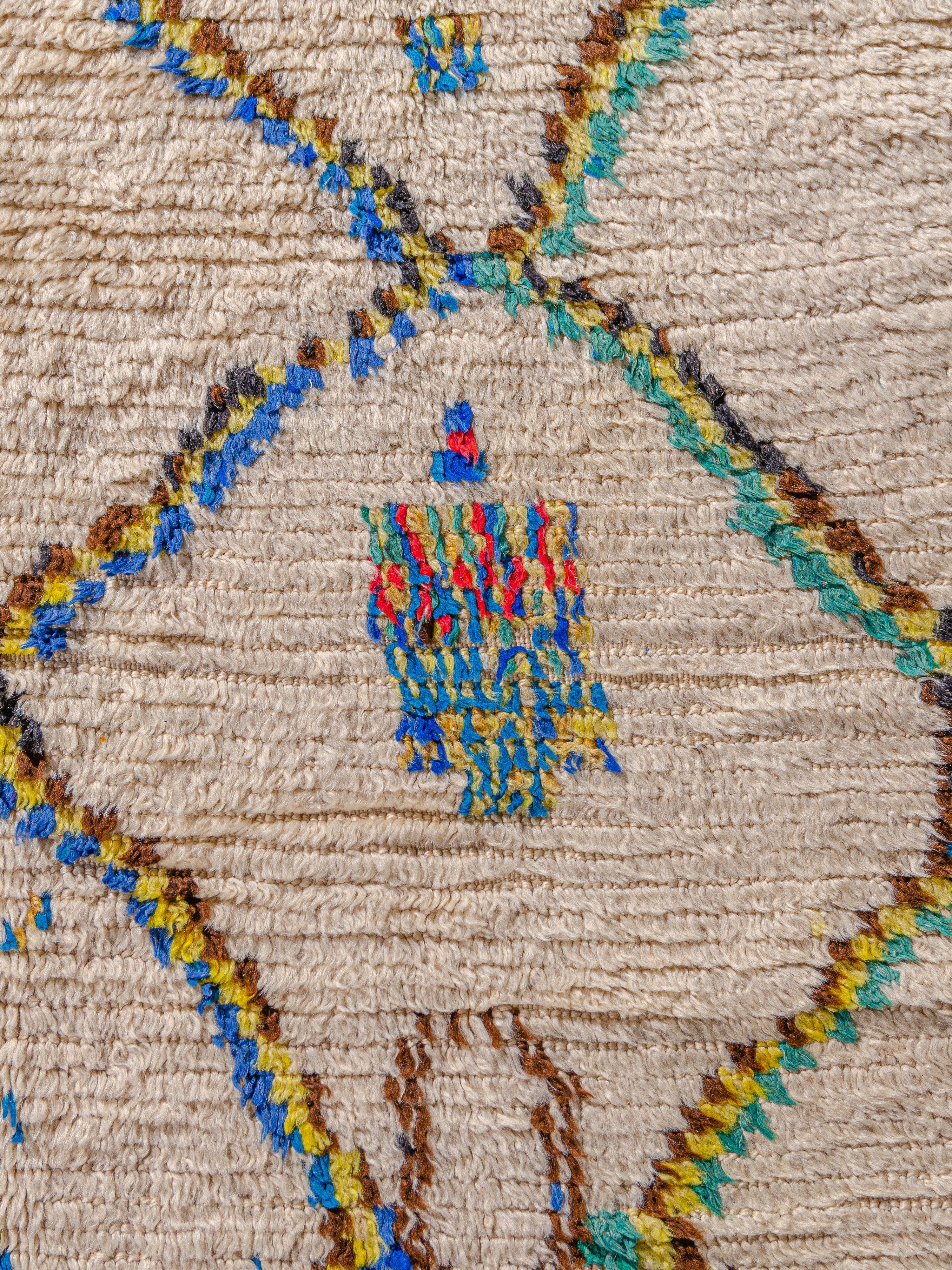 Un exceptionnel azilal marocain vintage avec un réseau de losanges distinct combiné à des motifs abstraits flottants dans tout le champ. Noué dans une palette vivante de turquoise, jaune, bleu électrique, rouge et brun naturel sur un fond ivoire. Un
