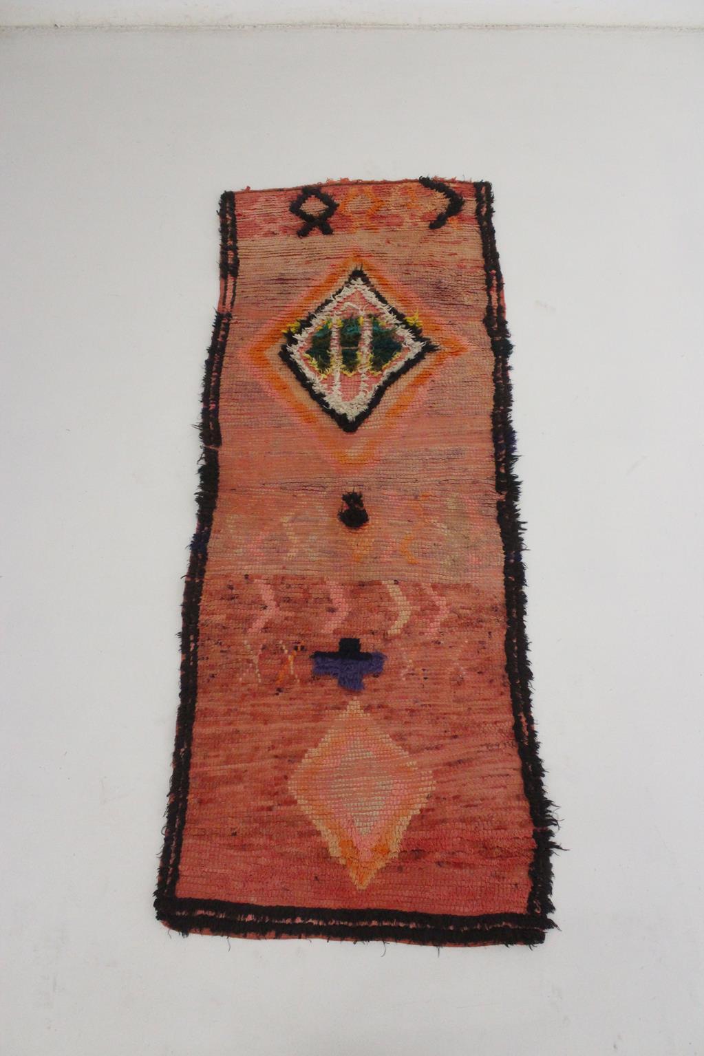 Dieser Vintage-Läufer bringt die perfekte Bohème-Stimmung in Ihren Raum! Der Teppich, der wahrscheinlich in der Gegend von Boujad im Mittleren Atlas in Marokko hergestellt wurde, zeigt einen pfirsichrosa Hintergrund mit einem schwarzen Rahmen und