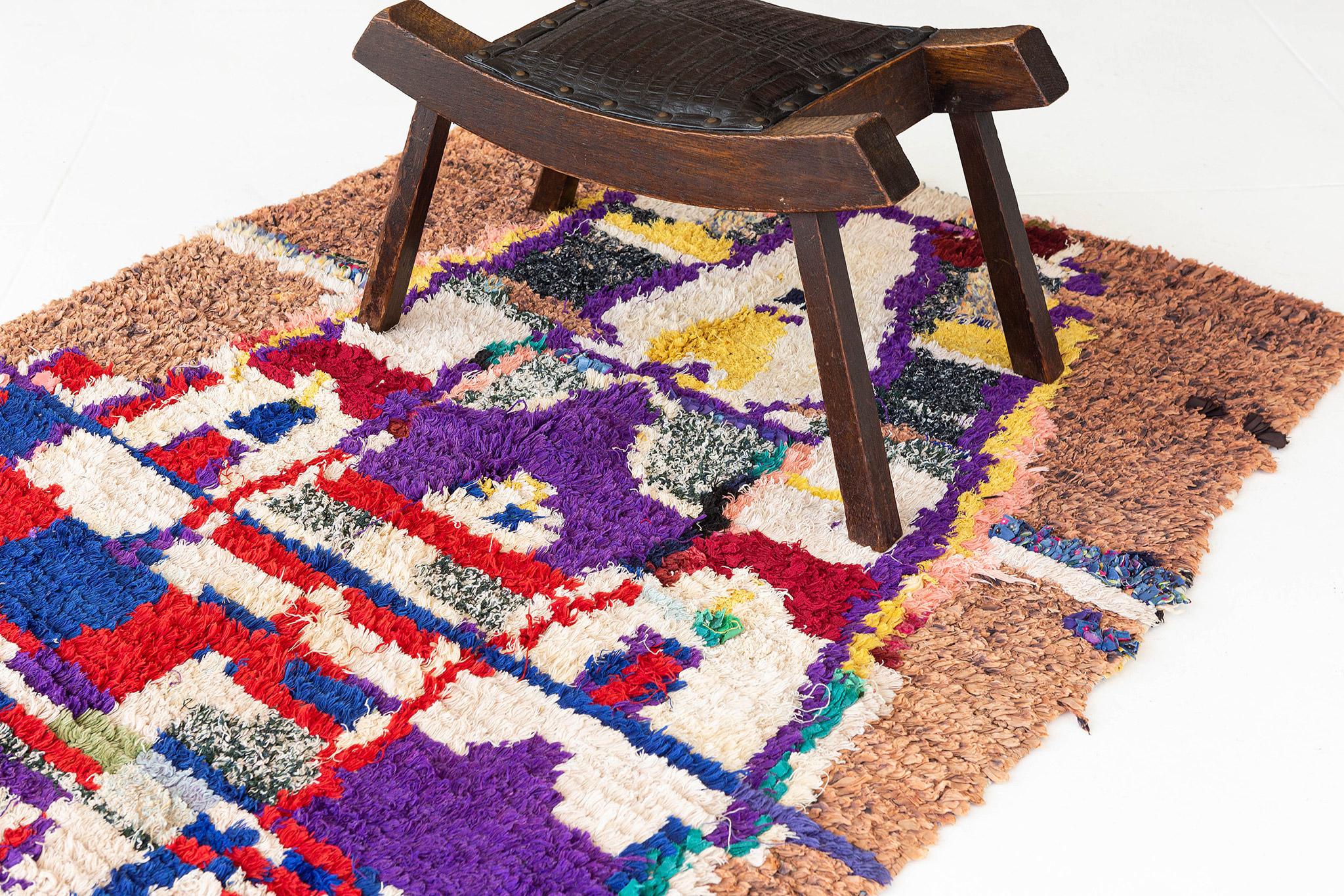 A rug like a painting! A white shape area seems to emerge from a ground plane at the bottom of the rugwith . It is filled with multi-colored shape elements of purple, red, blue and yellow. A variegated brown and clay-colored field suggests