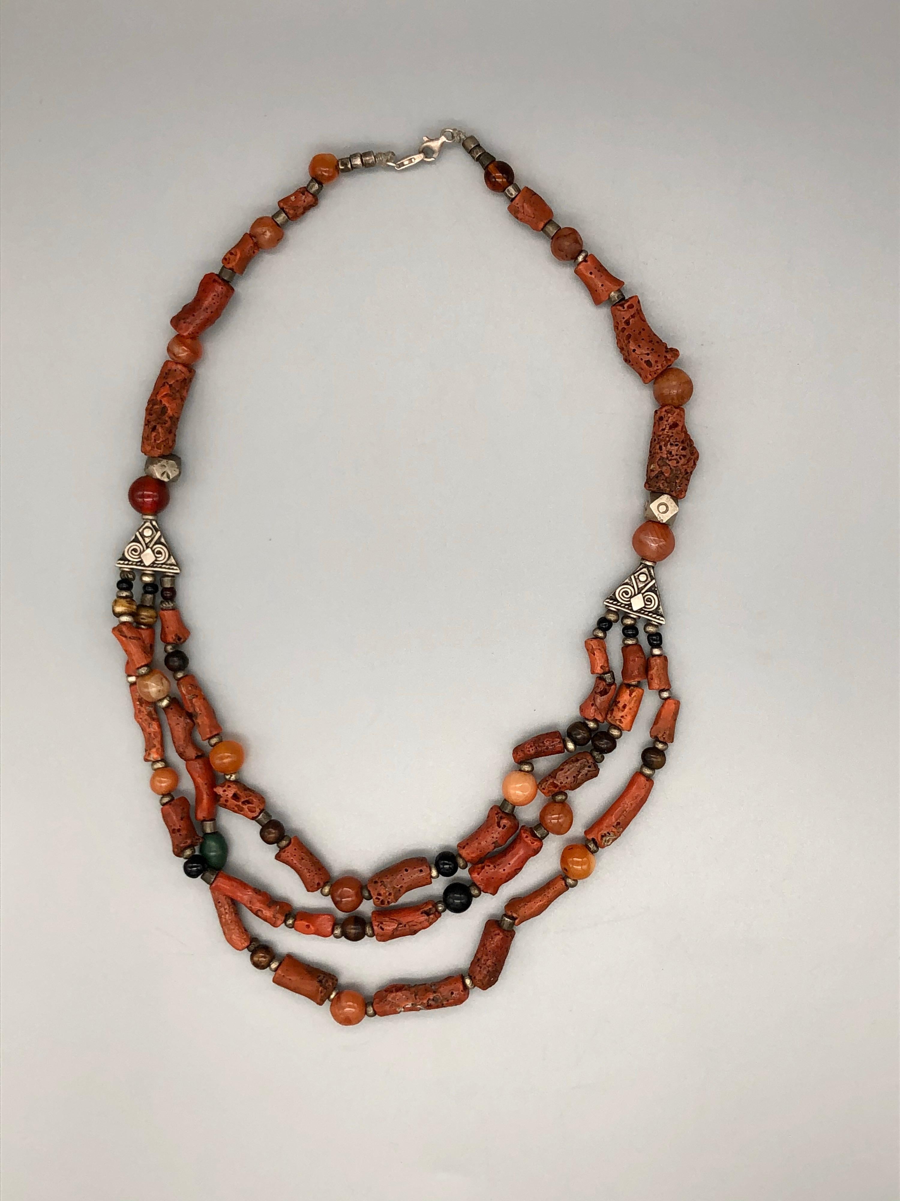 This vintage coral necklace is a wonderful find. Large pieces of true red branch coral are interspersed with agate stones and etched and stamped silver beads. Other beads include tiger's eye, onyx, and glass. Three strands meet on sides in a