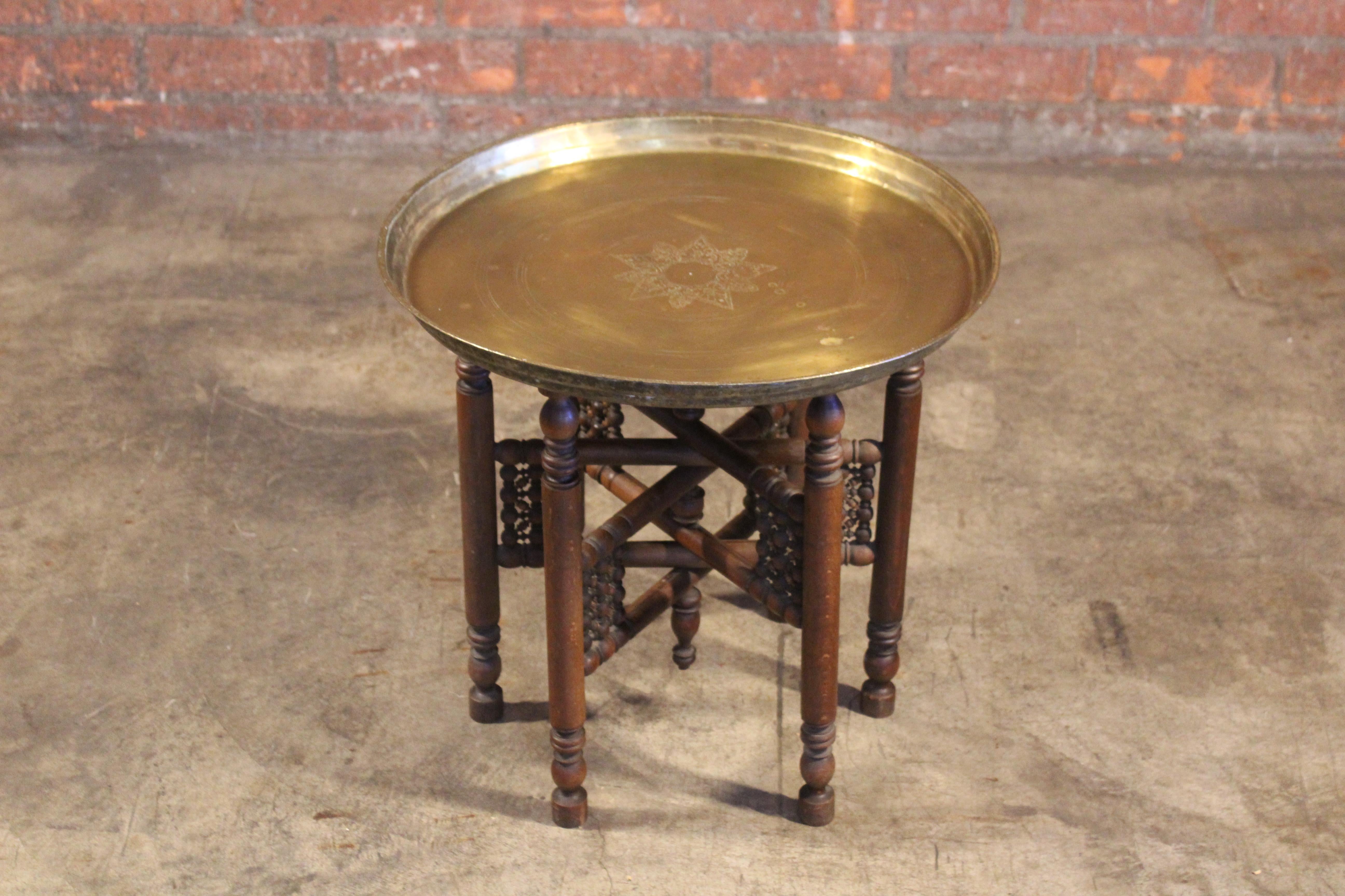 A vintage brass tray table on a folding carved wooden base, Morocco, 1970s. In good condition with age appropriate wear.