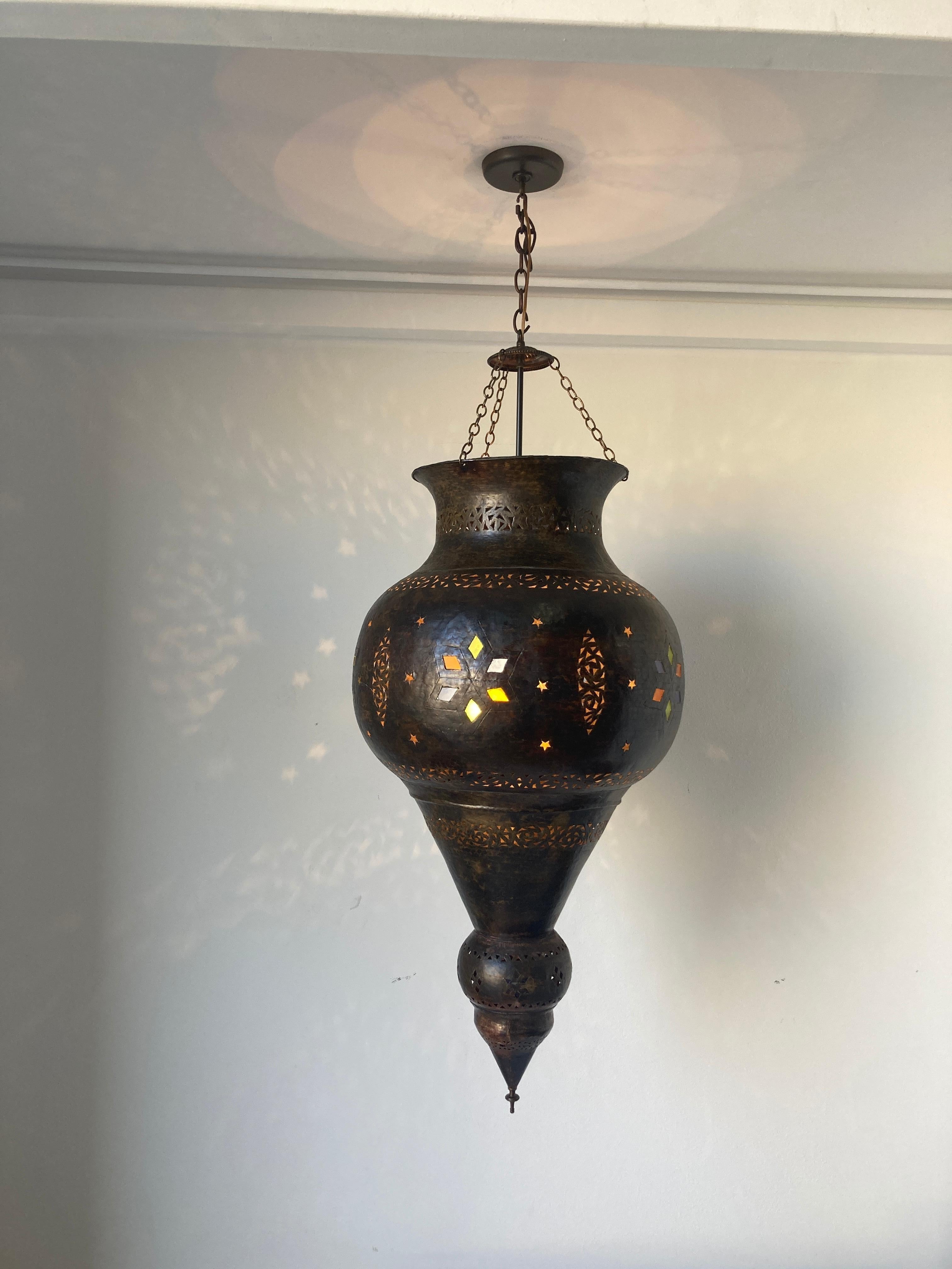 Vintage Moroccan large bronze patinated pendant.
This large Moorish bronze chandelier is delicately hand-crafted and hand-hammered with openwork design with small jeweled colored glass.
Rewired ready to install, comes with matching color ceiling