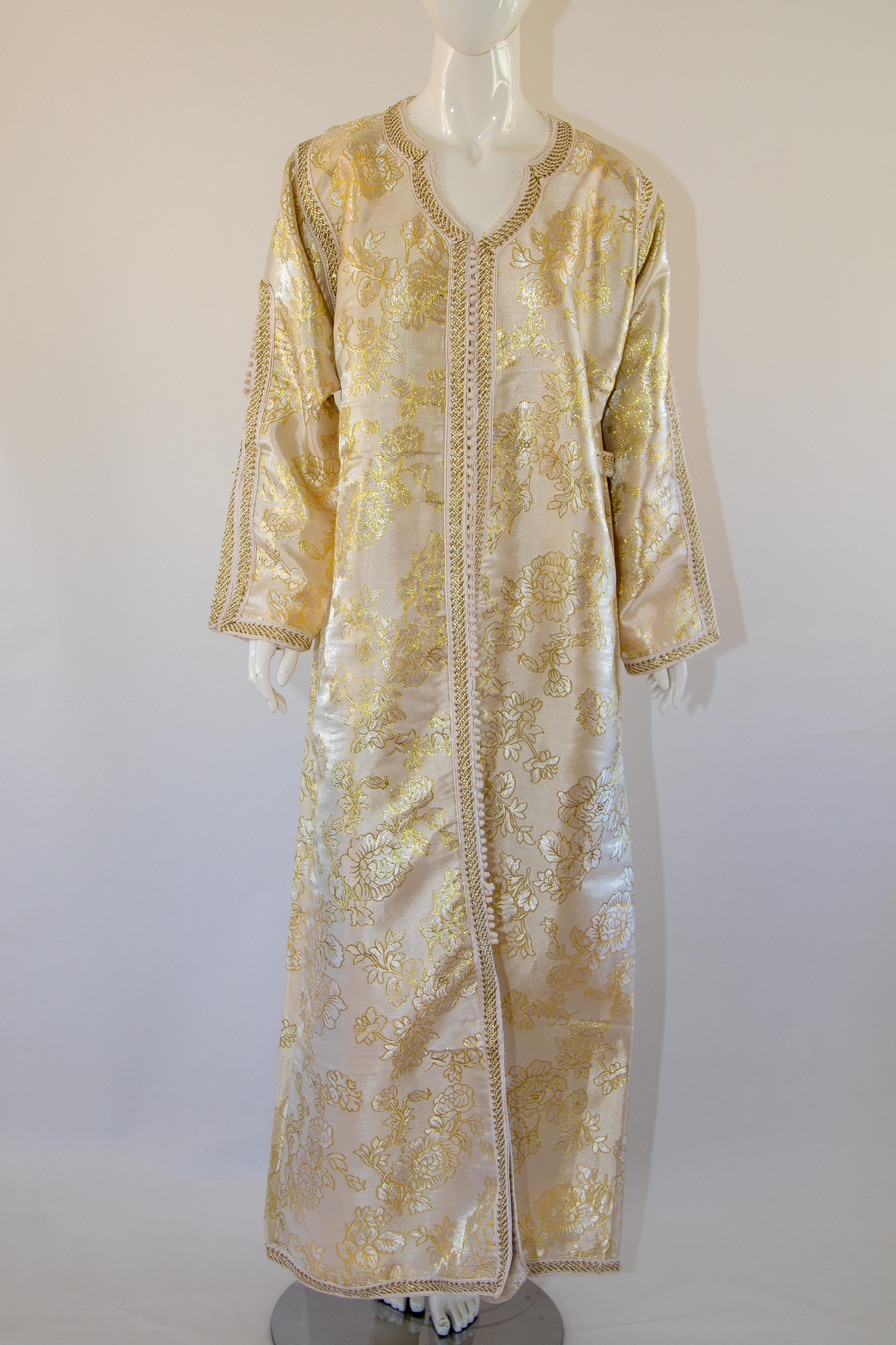 Moroccan vintage exotic metallic white gold brocade caftan gown, circa 1970s.
The luxurious Moorish kaftan is designed with white and gold metallic brocade.
The front of the elegant caftan gown is embellished at the front with woven gold buttons and
