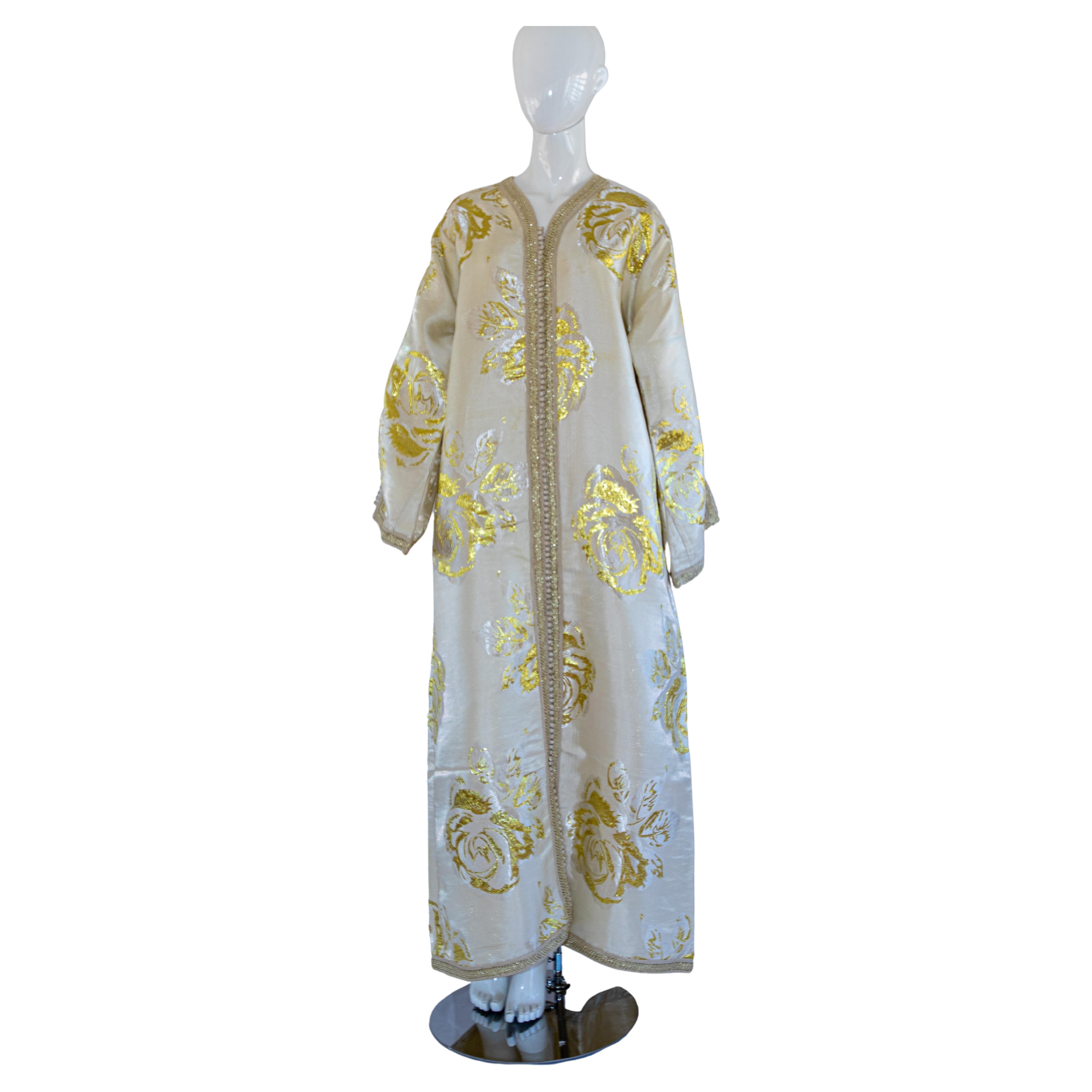 Vintage élégant caftan marocain blanc et or lame métallique brocart floral,
vers les années 1970.
Confectionné au Maroc, il est taillé pour une coupe décontractée et des manches larges.
Cette longue robe maxi kaftan vintage est brodée et embellie