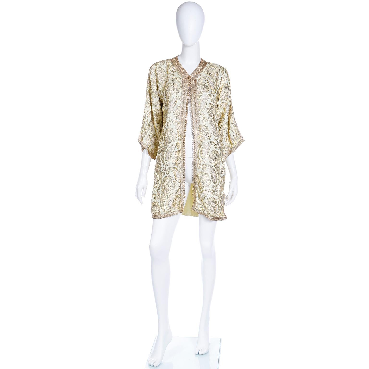 This is a vintage Moroccan Ottoman ivory gold metallic embroidered caftan style jacket in a gorgeous ornate paisley pattern. This versatile jacket has intricate gold braid trim and gorgeous knotted gold fabric buttons with loop closures. 

We love