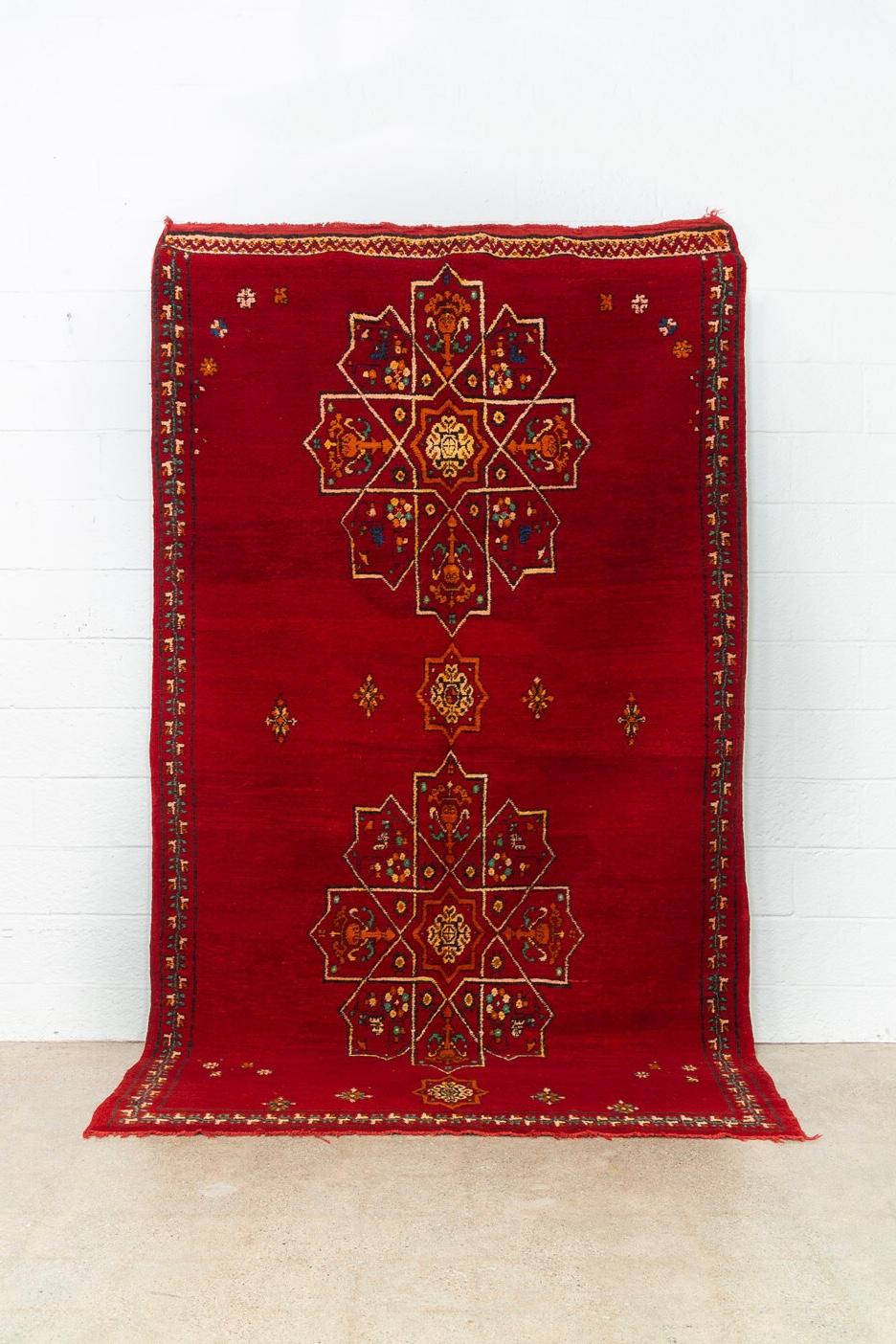 This stunning large vintage handwoven Moroccan Berber rug circa mid-20th century is a beautiful combination of hand knotted pile and embroidery. The design features a large symmetrical arabesque pattern on a gorgeous field of crimson red with accent