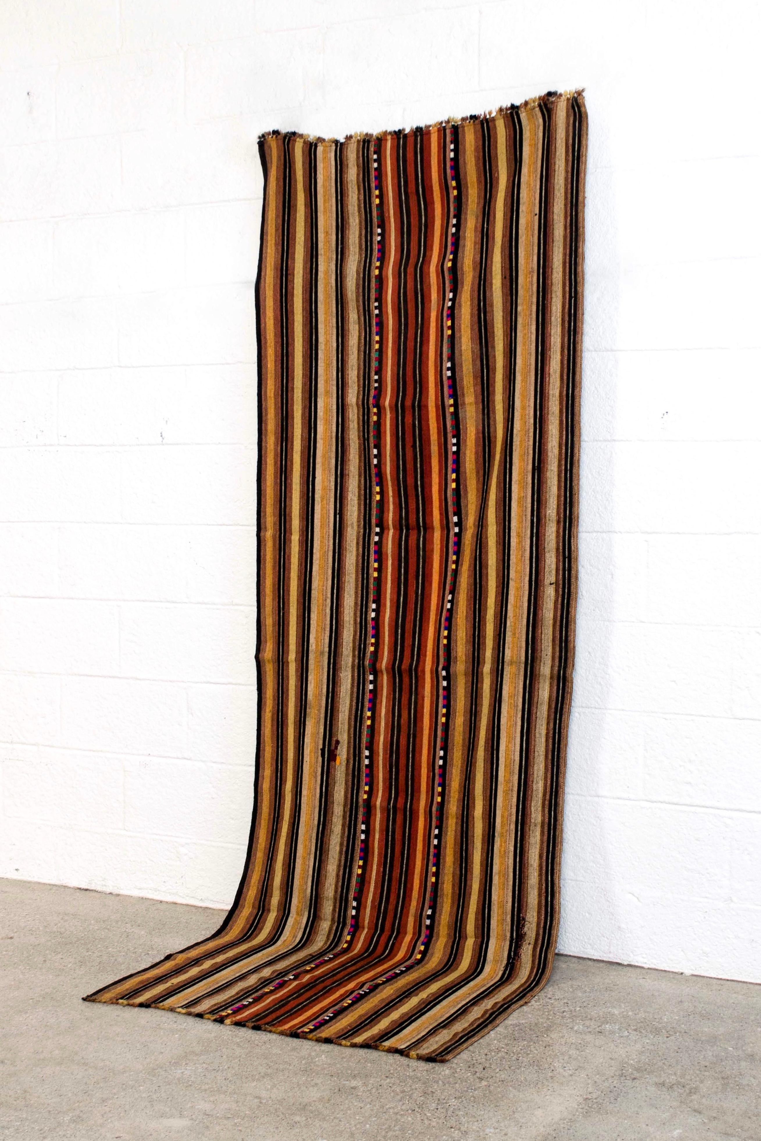This vintage handwoven Moroccan Berber rug runner is handcrafted from hand spun wool and cotton. It features vertical stripes in a color palette that includes brick, black, ivory, burnt orange, mustard and camel with two thin center stripes of