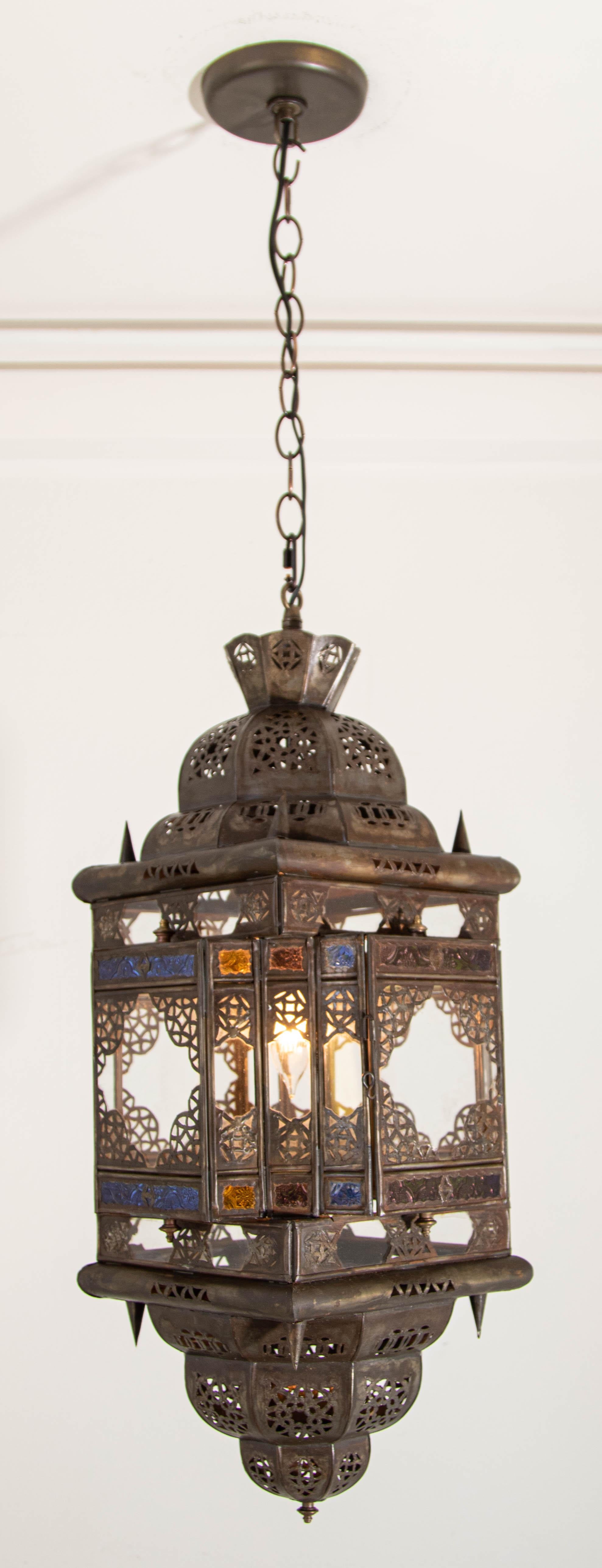 Lanterne suspendue marocaine vintage en verre clair et multicolore fabriquée à Marrakech
Pendentif lanterne en verre clair et multicolore de forme carrée, fabriqué à la main par des artisans marocains à Marrakech.
Le métal est découpé à la main dans