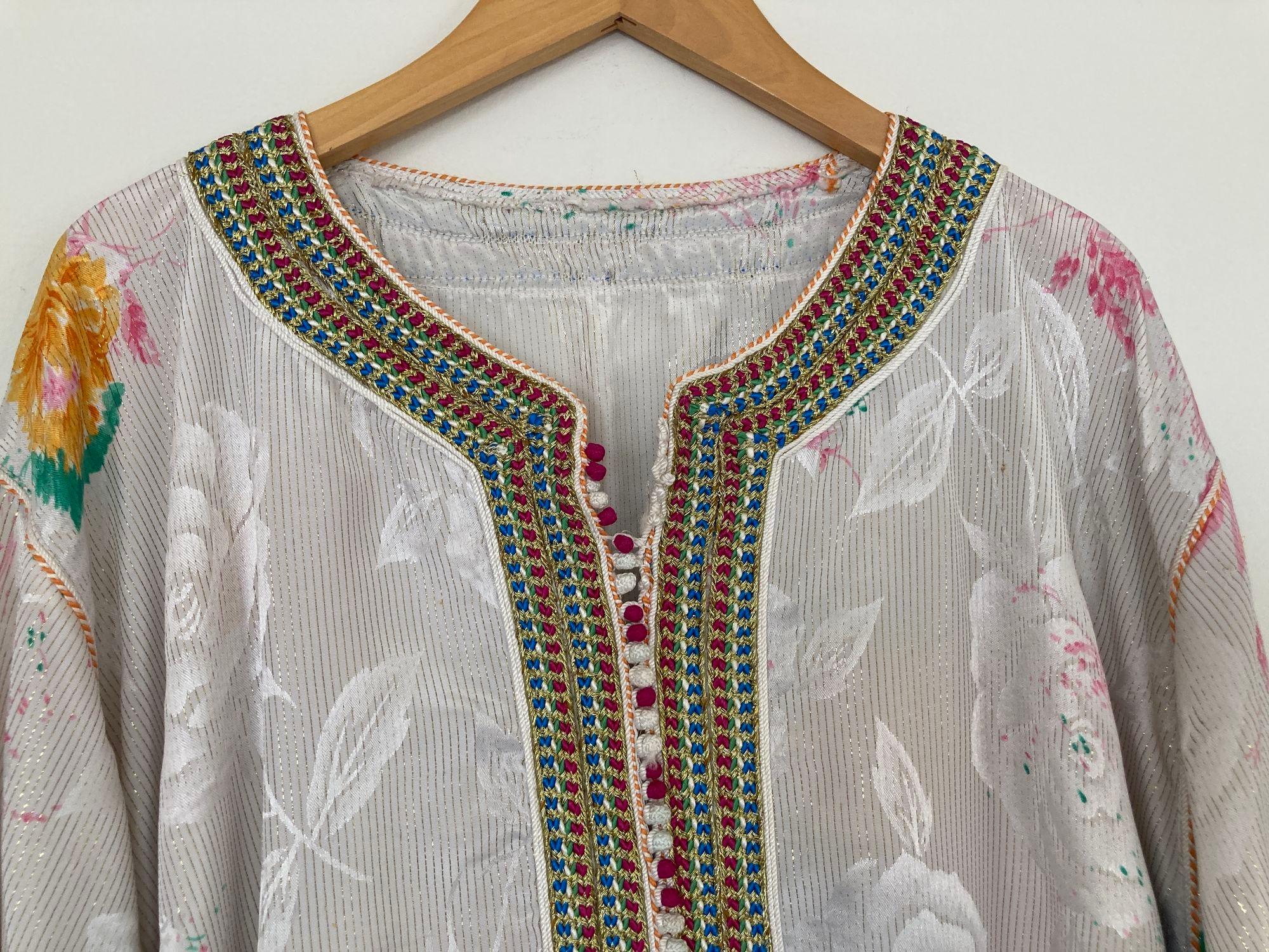 Eleganter marokkanischer Kaftan in weißem Blumendesign mit goldfarbener Flechtstickerei,
ca. 1970er Jahre.
Dieser Kaftan im langen Maxikleid ist vollständig von Hand verziert.
Es wurde in Marokko gefertigt und hat eine entspannte