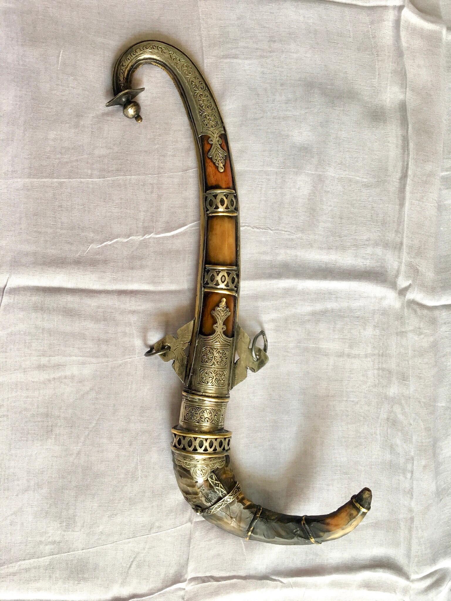 This vintage Moroccan dagger is known as a Khanjar. It has a curved metal blade, with a handle made from gazelle Horn and a sheath of camel bone. The metalwork is silver melange, intricately hand-etched with beautiful and detailed designs. Two rings