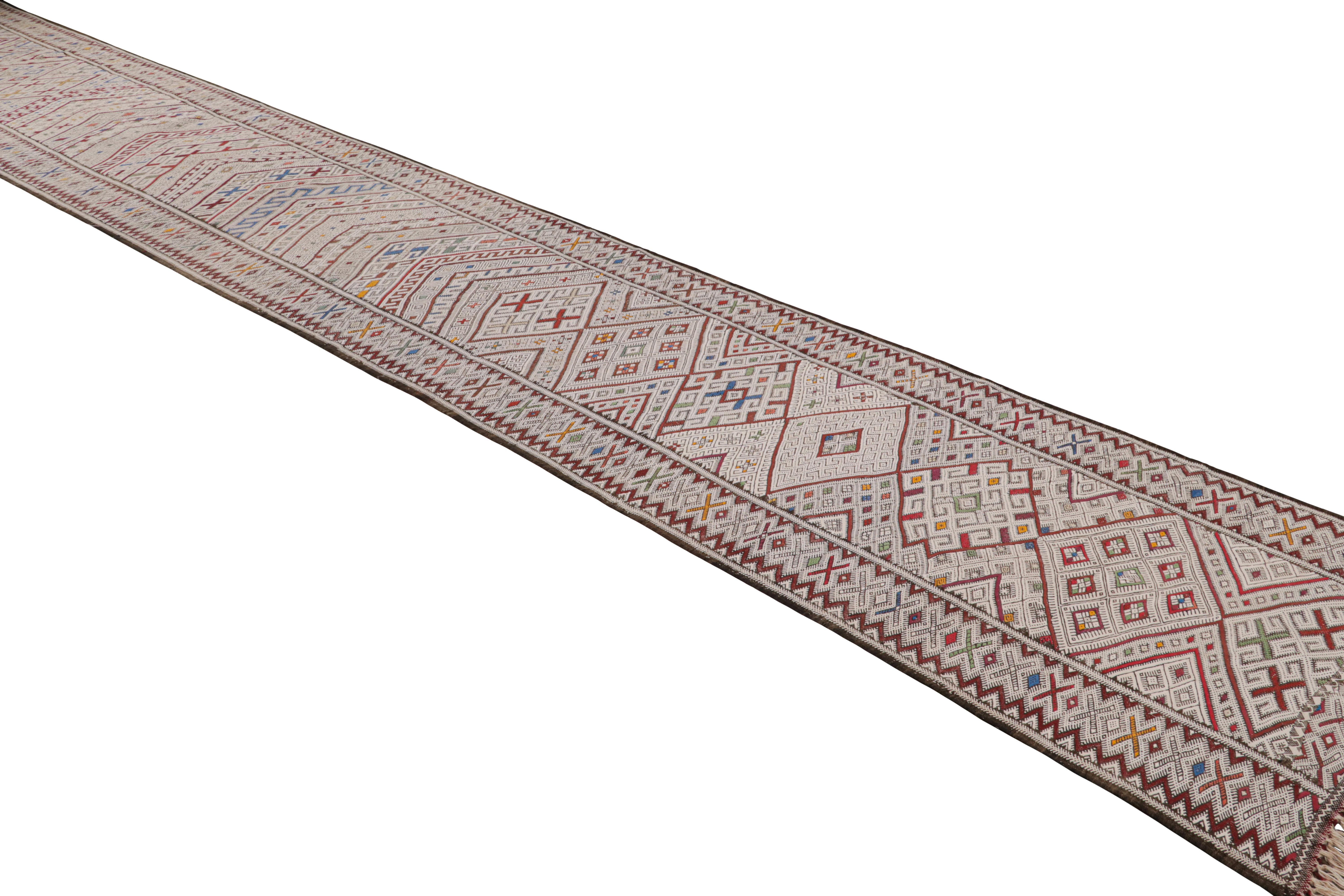 This 3x23 vintage Moroccan kilim runner is a Zayane rug from the tribe of the same name–handwoven in wool circa 1950-1960.

On the Design:

This flatweave enjoys patterns in polychromatic colorways, with notably present white and brown tones among