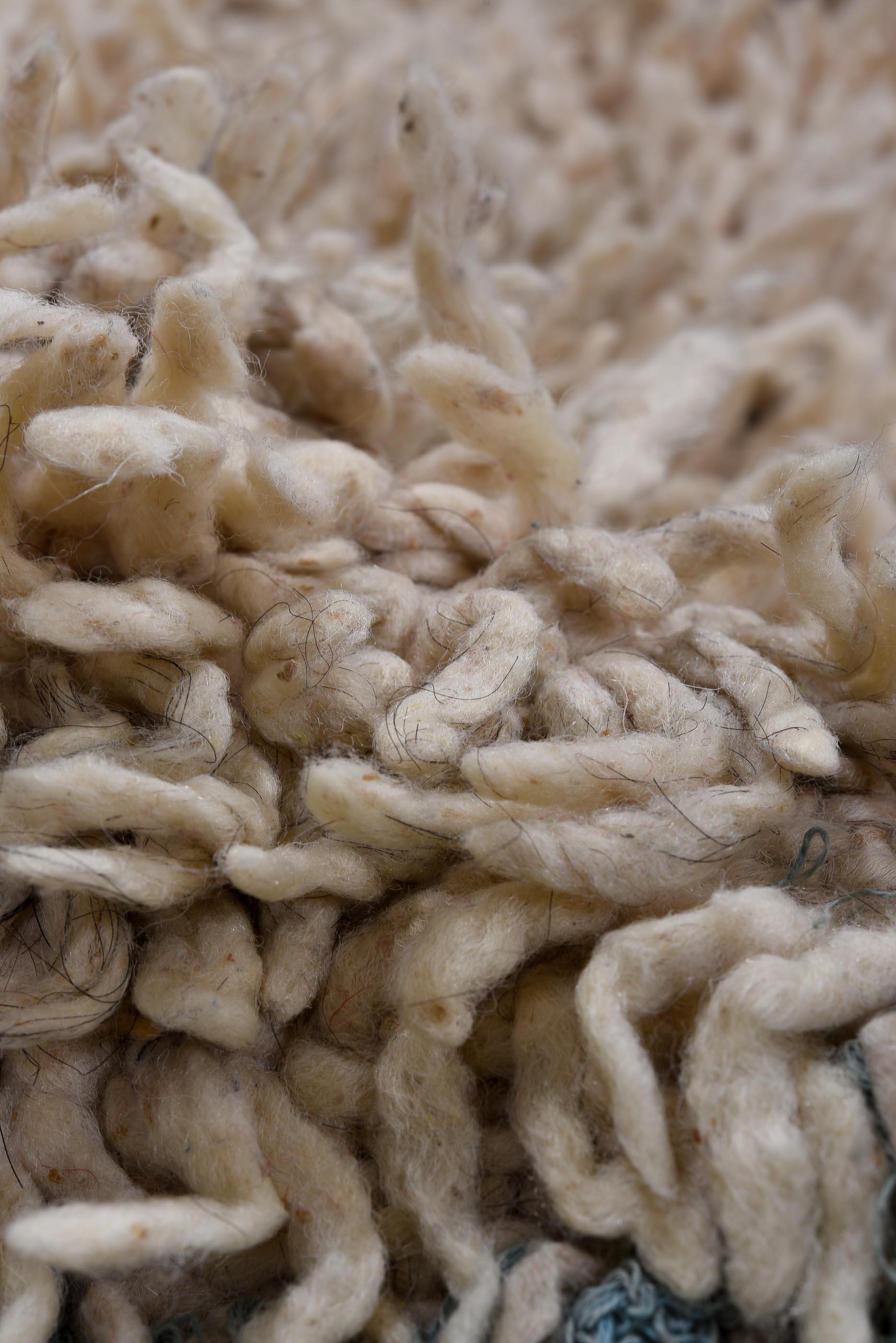 Esta alfombra marroquí vintage presenta un campo afelpado de tonos crema salpicado de motivos abstractos simétricos en añil oscuro, ocre suave y negro, creando una equilibrada interacción de simbolismo bereber tradicional y minimalismo moderno. La