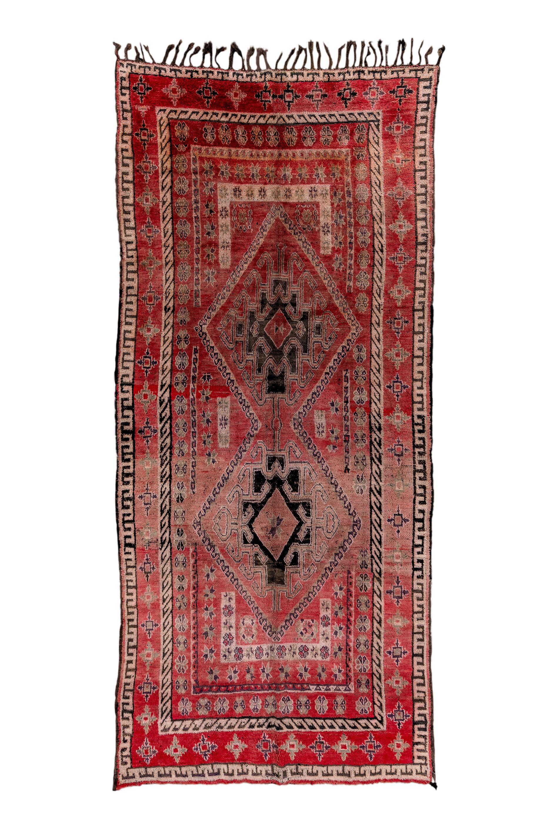 This lowland Moroccan kellegi (long carpet) partakes slightly in a Southwest Persian aesthetic with two conjoint rust lozenges, each containing a version of the “Qashghai gul”, all on the rust field. An ecru bracket at each field end positions the