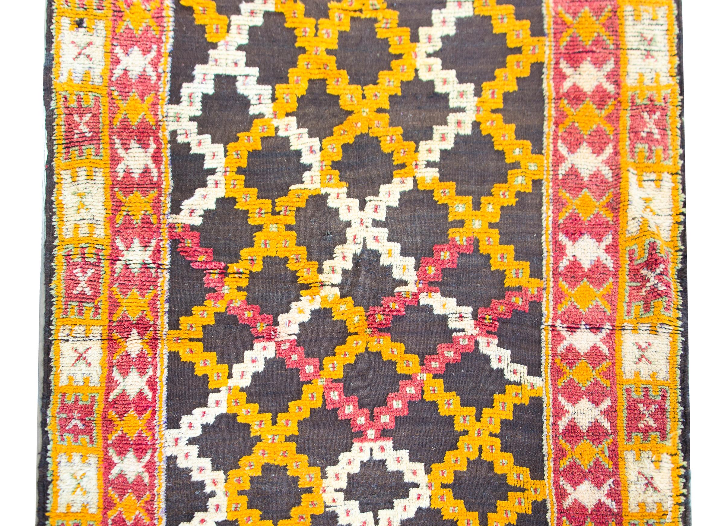 A wonderful mid-20th century Moroccan rug with a trellis pattern woven in gold, white, and crimson, set against a black background, and surrounded by a border with two distinct stylized floral patterned borders.