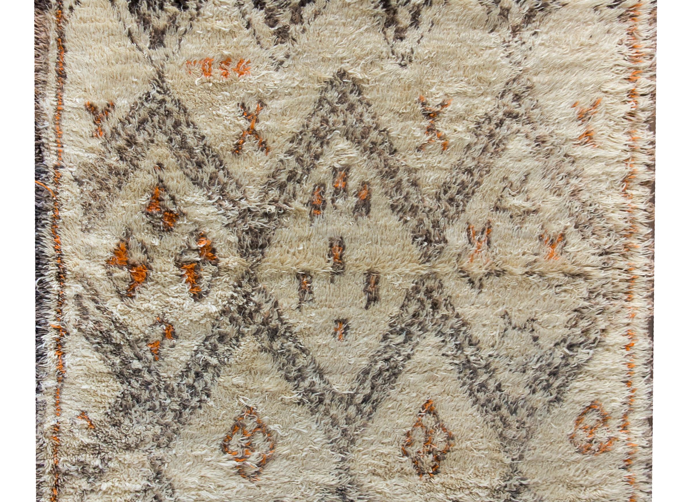A chic and bold mid-20th century Moroccan rug with an all-over geometric partner including large and small diamonds on one end, and zigzag stripes on the other, and all woven in brown and orange wool set against a natural cream colored wool ground.