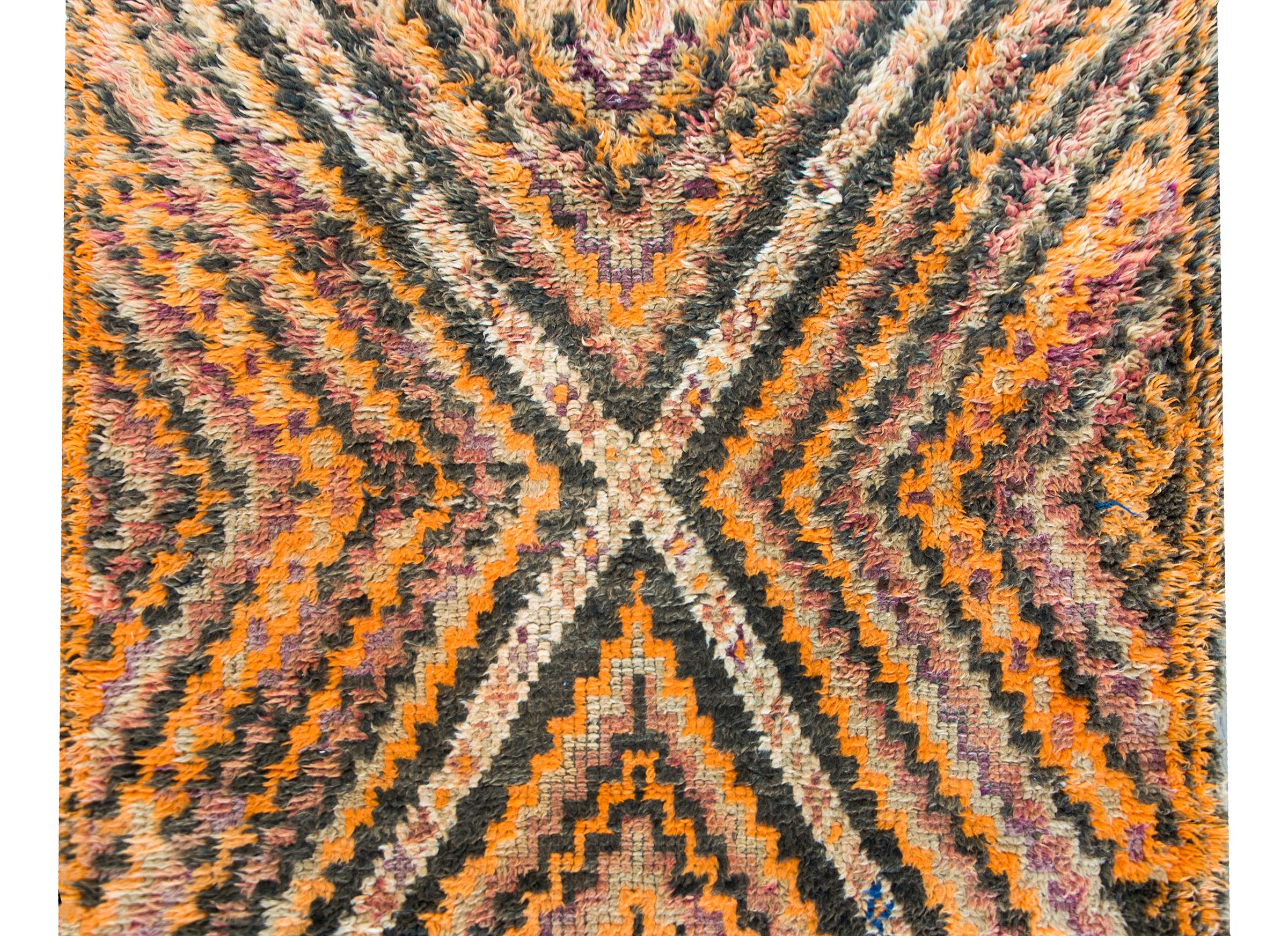A wonderful mid-20th century Moroccan rug with an all-over zigzag pattern created from alternating black, orange, violet, and cream colored stripes creating a large diamond on one end.