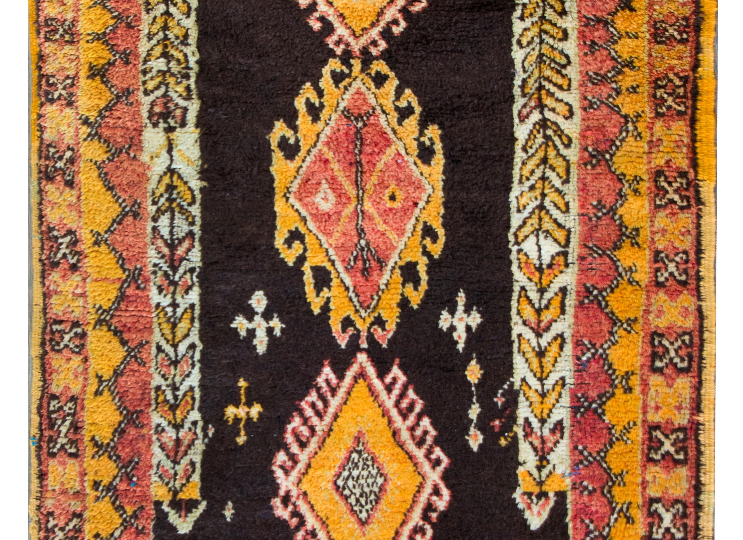A wonderful mid-20th century Moroccan rug with three large central diamond medallions with stylized floral borders, set against a brown background, and all circled by a complex border with petite repeated geometric patterned stripes woven in