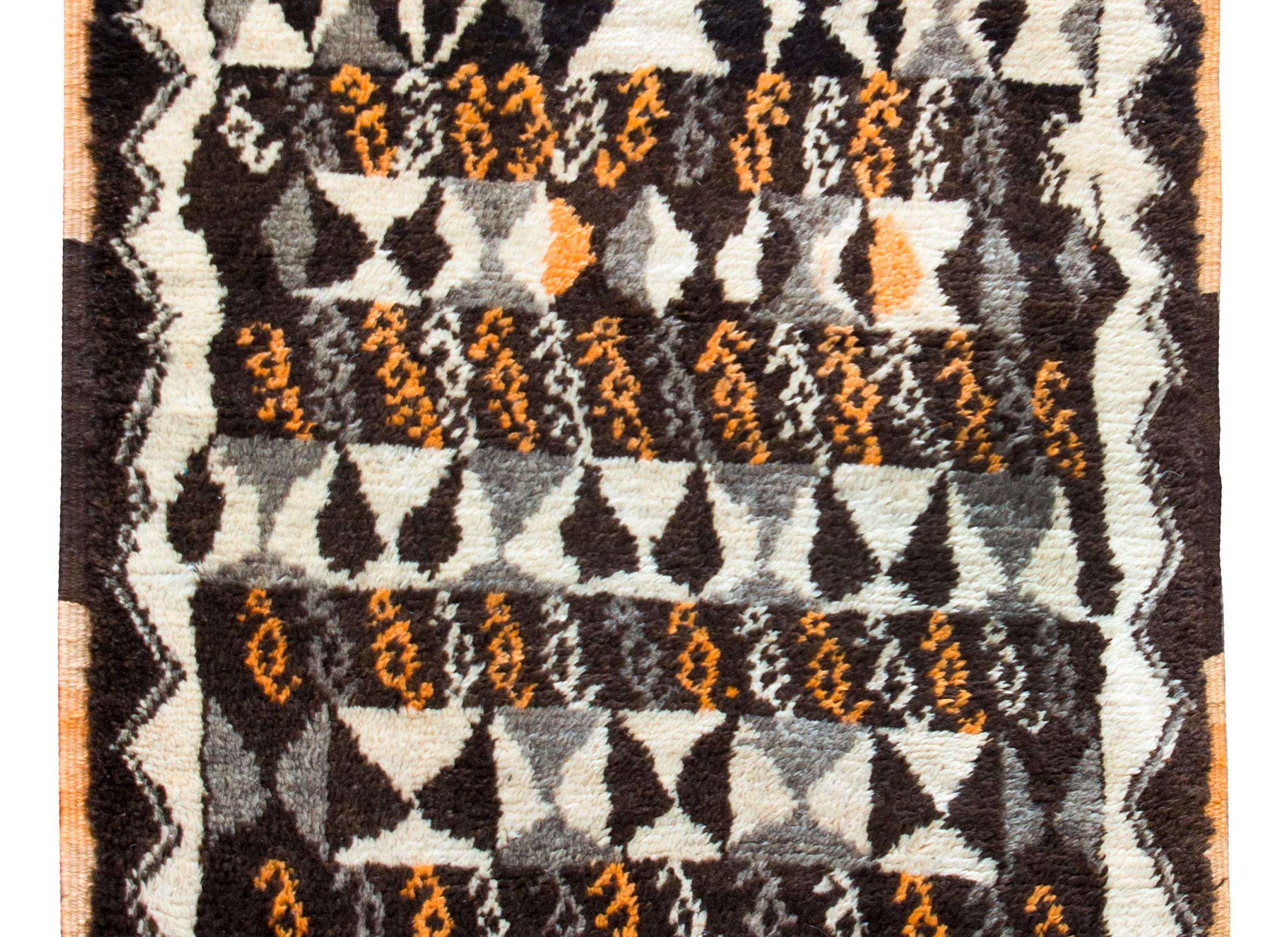 A chic vintage Moroccan rug with the best geometric pattern including myriad triangles in varying shades of gray, black, white, and orange, surrounded by a zigzag patterned border woven in similar colors as the field.