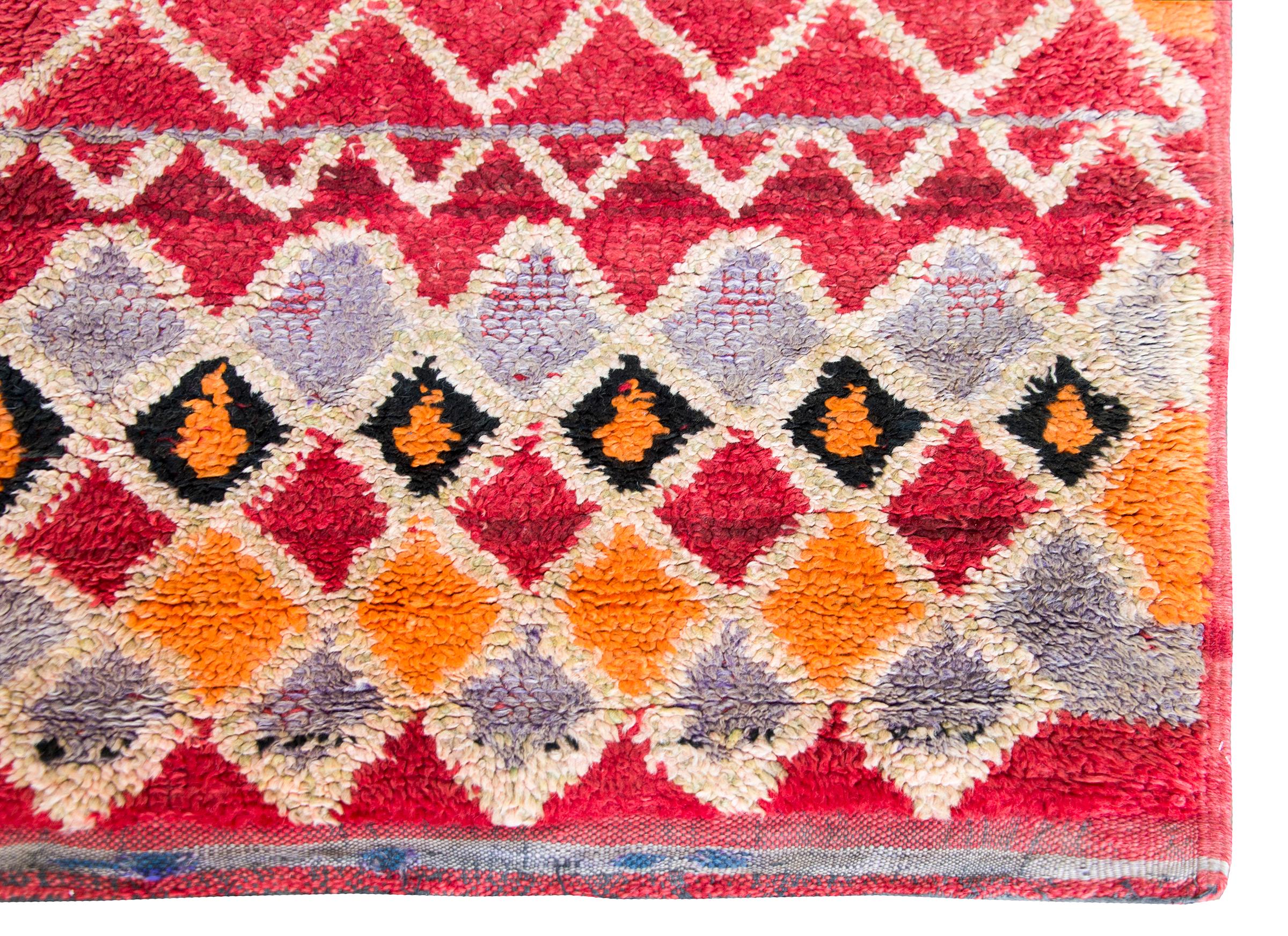 A bold and striking vintage mid-20th century Moroccan rug with an all-over diamond pattern woven in myriad colors including crimson, orange, pink, pale lavender, and black wool.