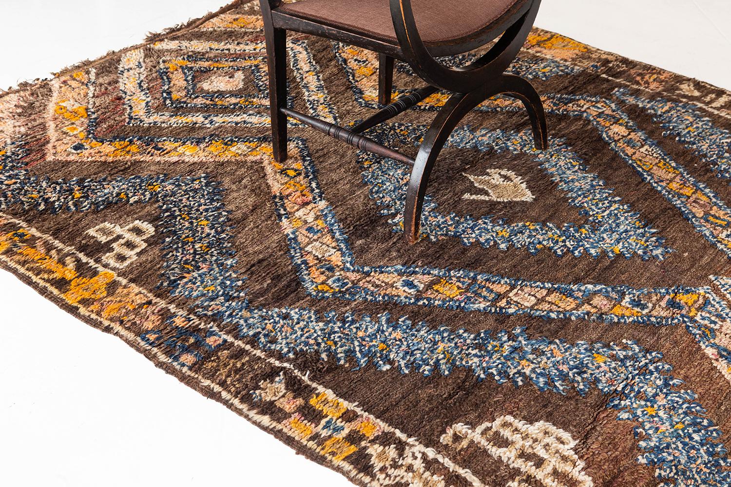 A vintage Moroccan from the High Atlas tribes of Morocco. This rug's has the perfect pile texture with a natural brown field. Blue, ivory and yellow make up the rug's tribal diamond design that in addition to the rug's symbolic traditional motifs.