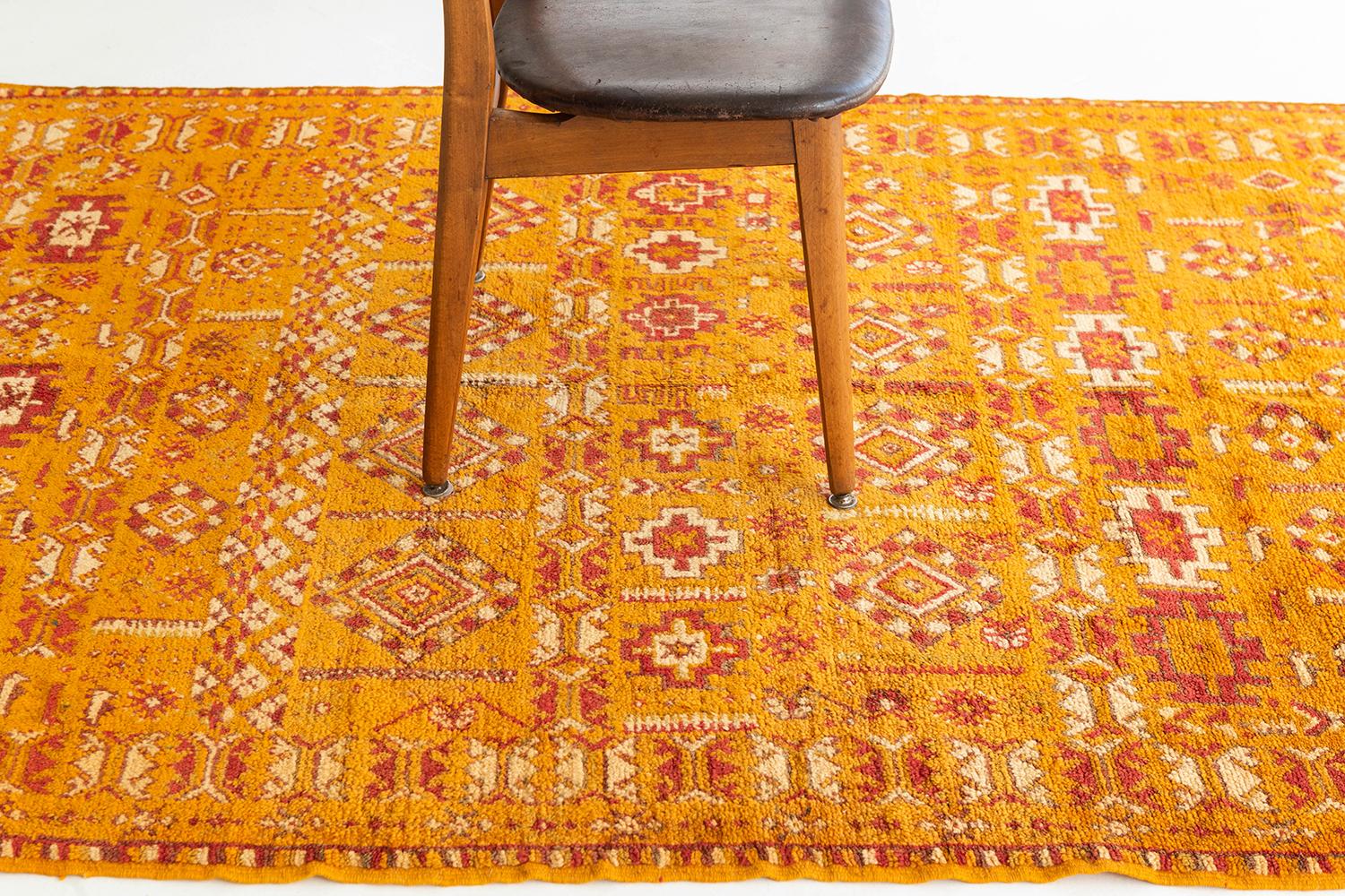 Saffron pile field with ivory and rich orange elements. All-over patterning with banded repeats and border motifs features archaic Berber symbols of prosperity and fortune in varied forms. A unique vintage tribal rug from the High Atlas Mountains of