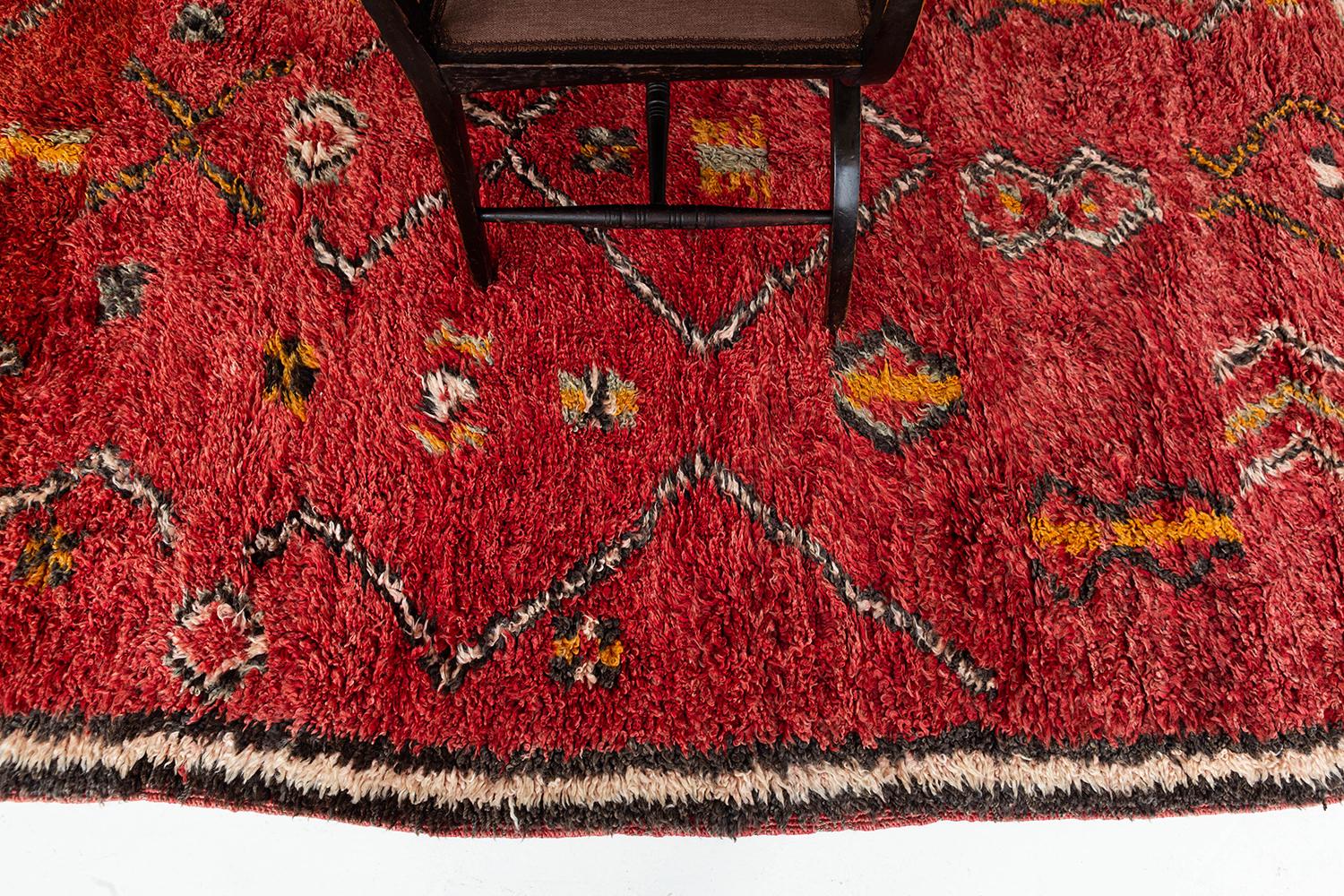 A bold and exciting vintage Moroccan from the High Atlas tribes of Morocco. Beautiful red shag surrounded by traditional and symbolic tribal motifs in saffron, black and ivory colors work together to create a perfect Moroccan rug. This rug's
