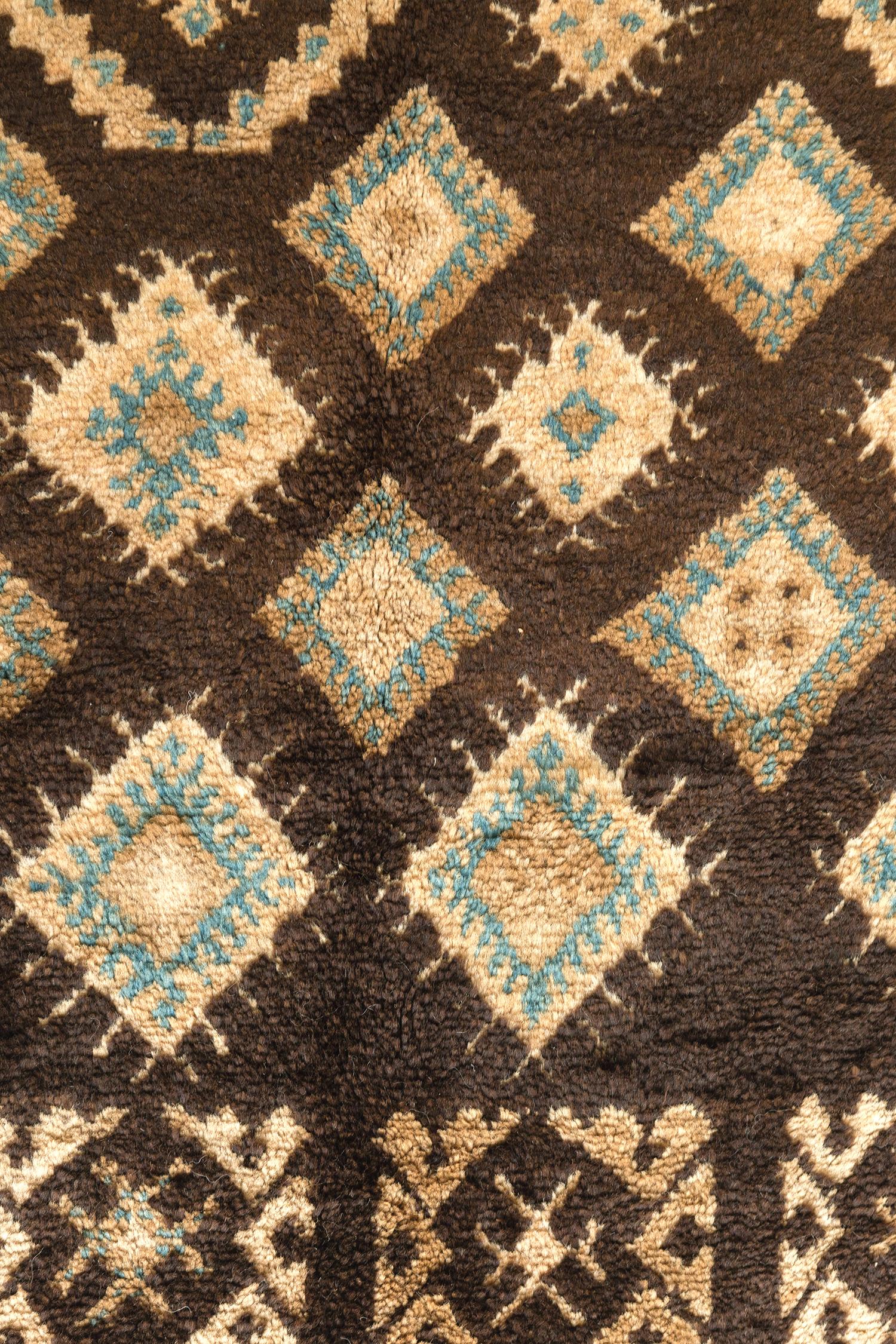 A majestic Vintage Moroccan High Atlas Tribe rug that features the stunning neutral tones of brown, ivory, camel and dusty blue. Embodying the fascinating all-over variations of symbolic lozenge panels, this masterful rug is enclosed with a border