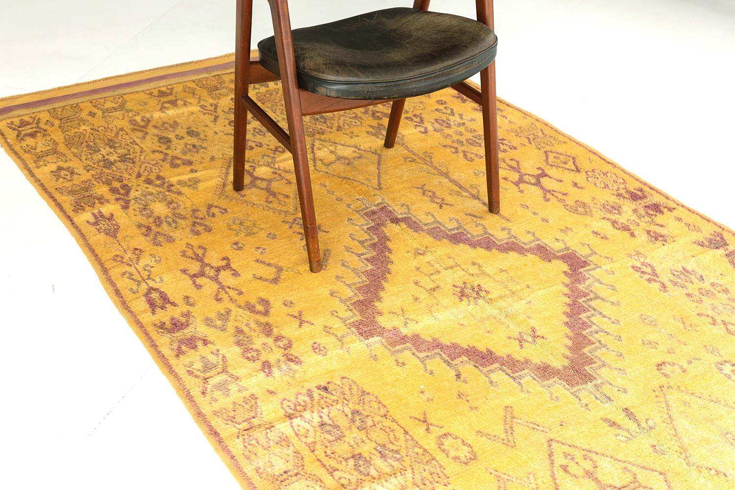 A vintage Moroccan rug in High Atlas Tribe Collection that features a central lozenge medallion surrounded by ambiguous symbolic Berber motifs running along the muted golden field. This remarkable rug is bounded with borders of intricate patterns of